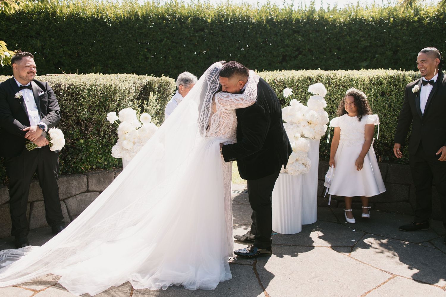 Wedding party poses together outdoors in formal attire with bridesmaids in white dresses and groomsmen in tuxedos.