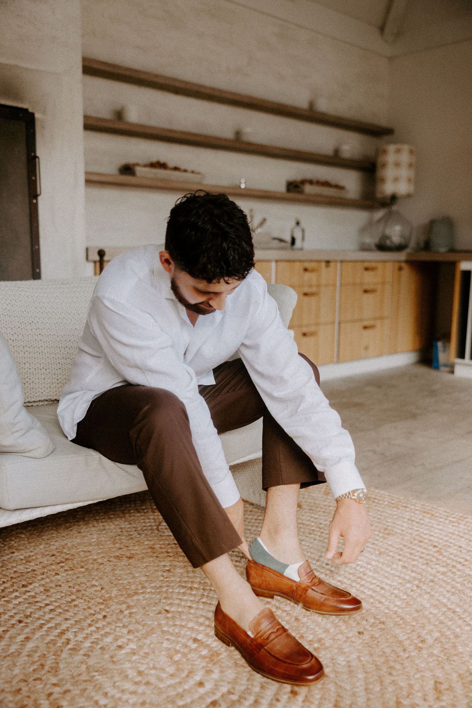 Close-up of someone putting on brown leather dress shoes on a textured carpet floor.