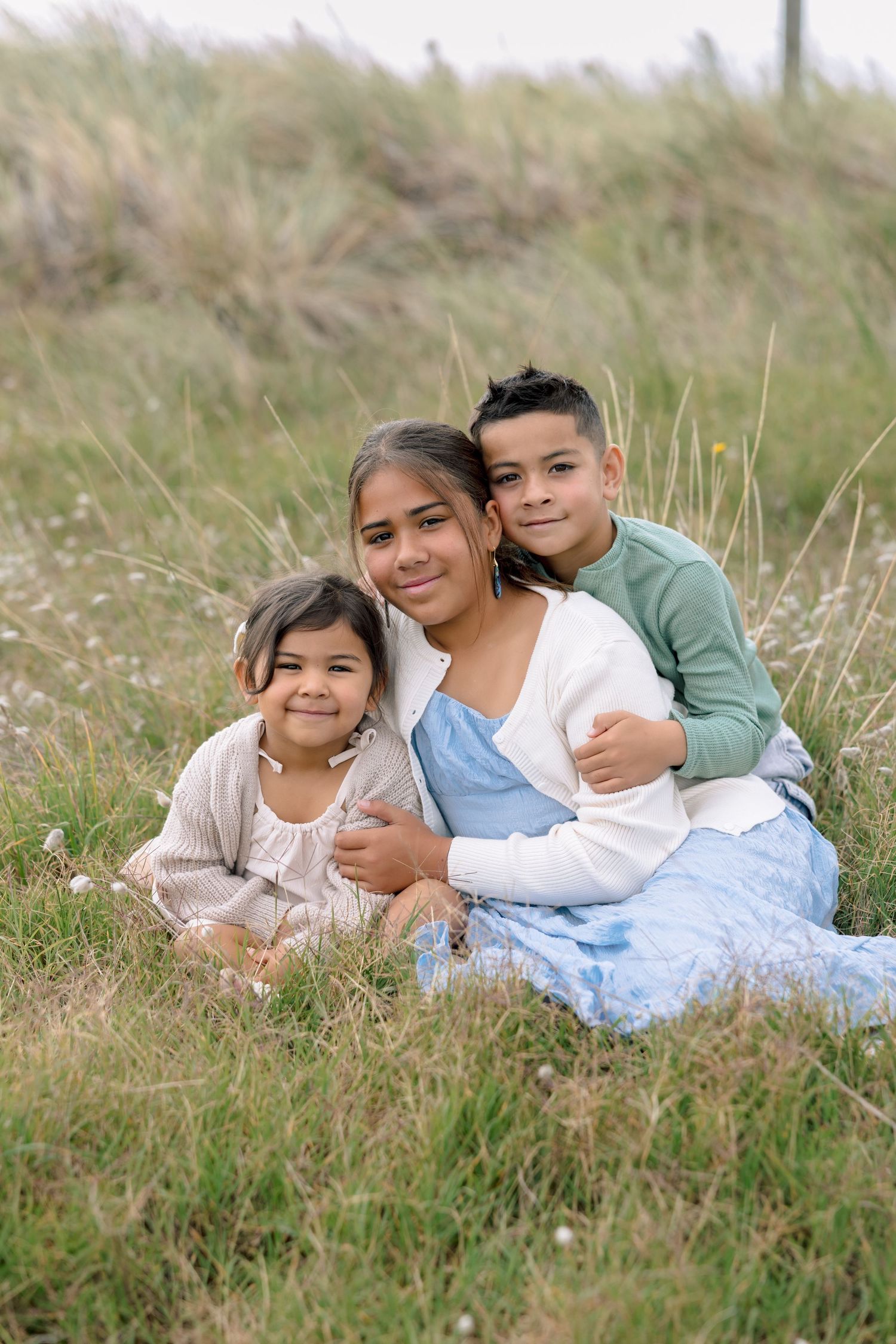 Family members lying together in tall grass on a hillside during an outdoor photo session.