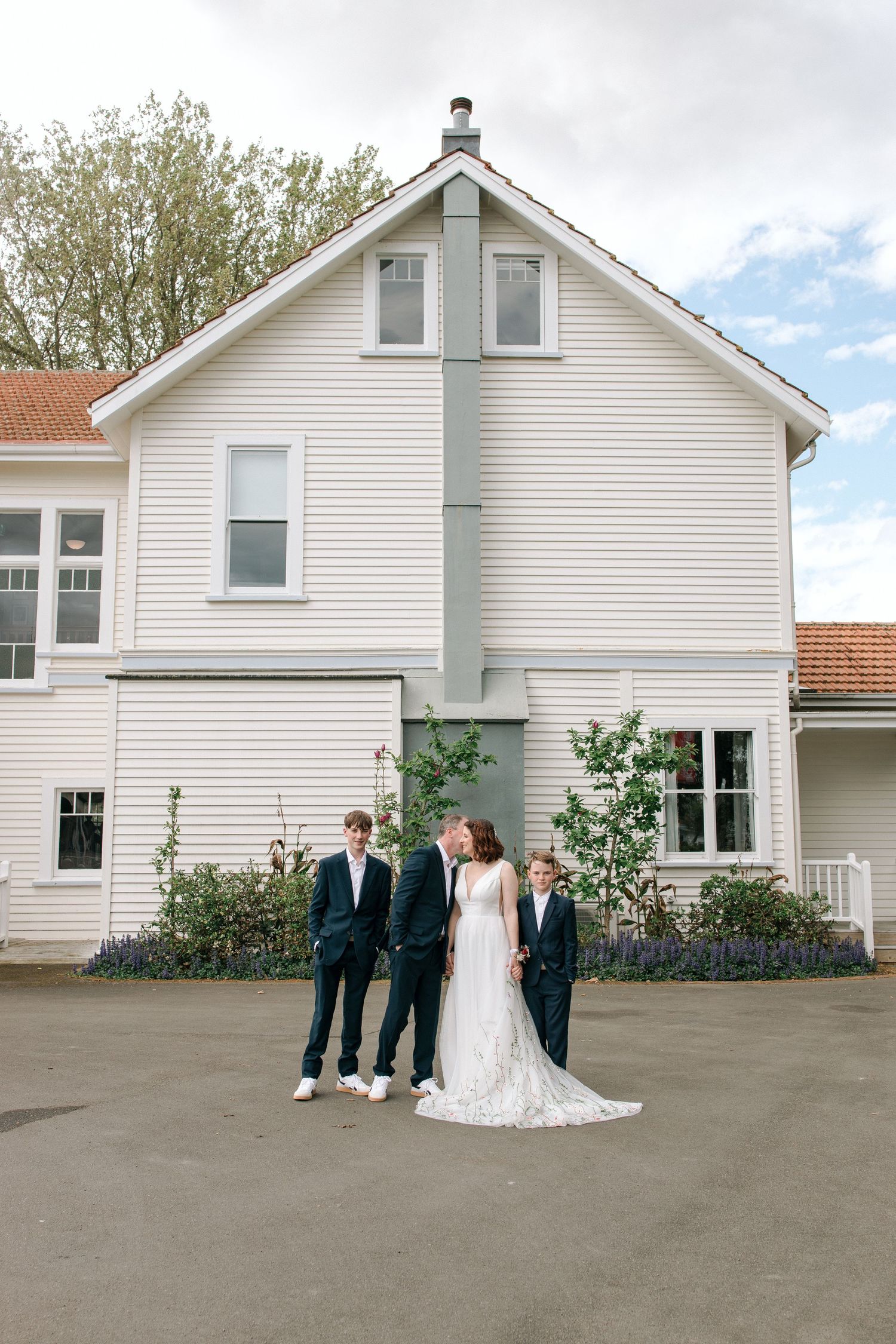 Wedding party standing in front of a classic white house with gray trim on an overcast day.