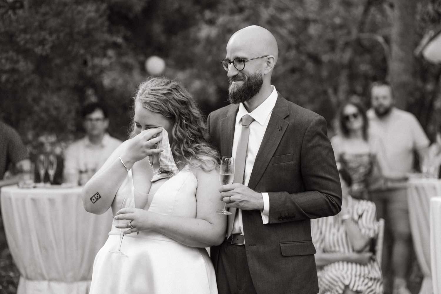 Black and white candid moment of emotional wedding reaction in outdoor setting.