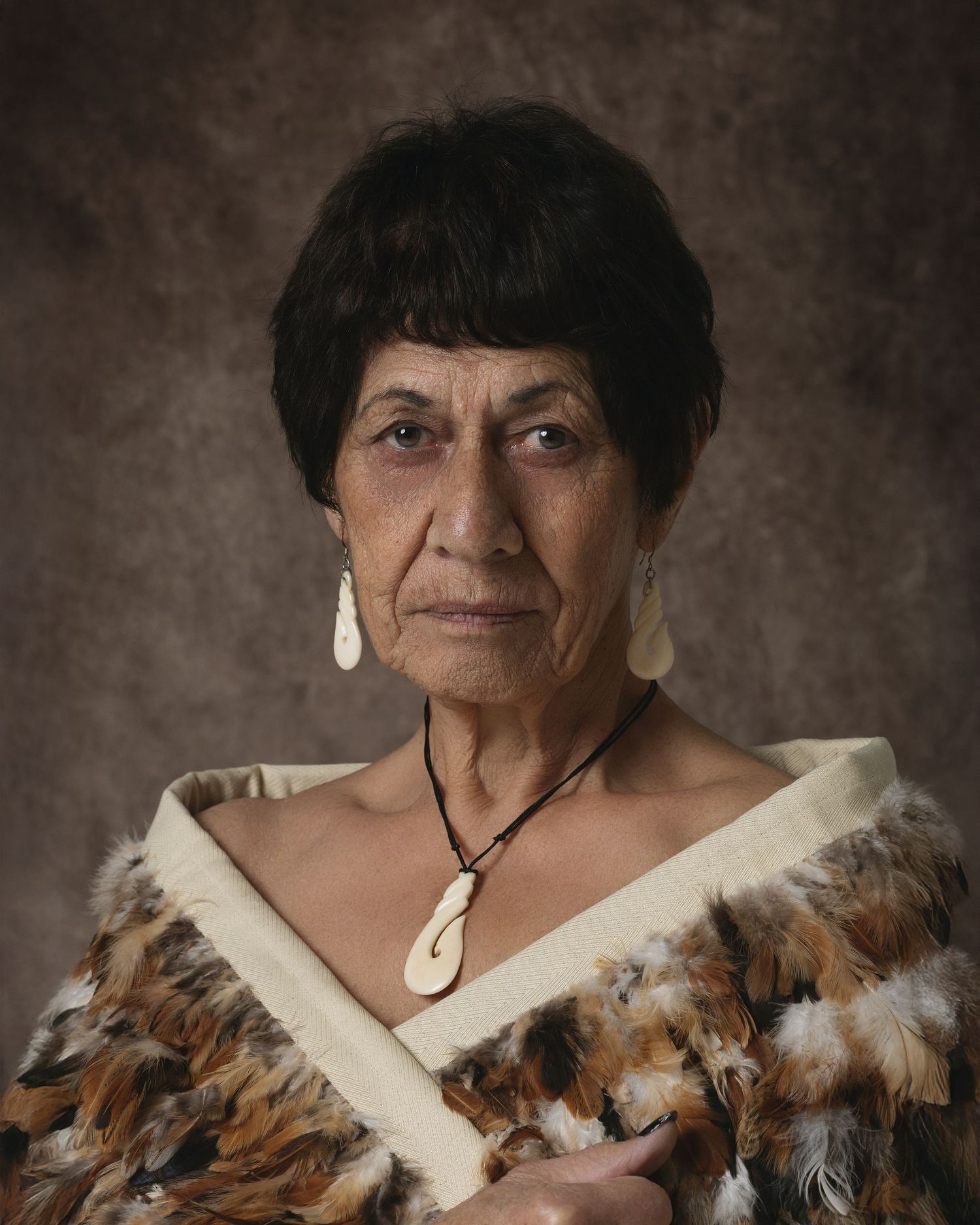 Maori woman in traditional feather cloak and bone hei matau pendant with shell earrings, formal portrait.