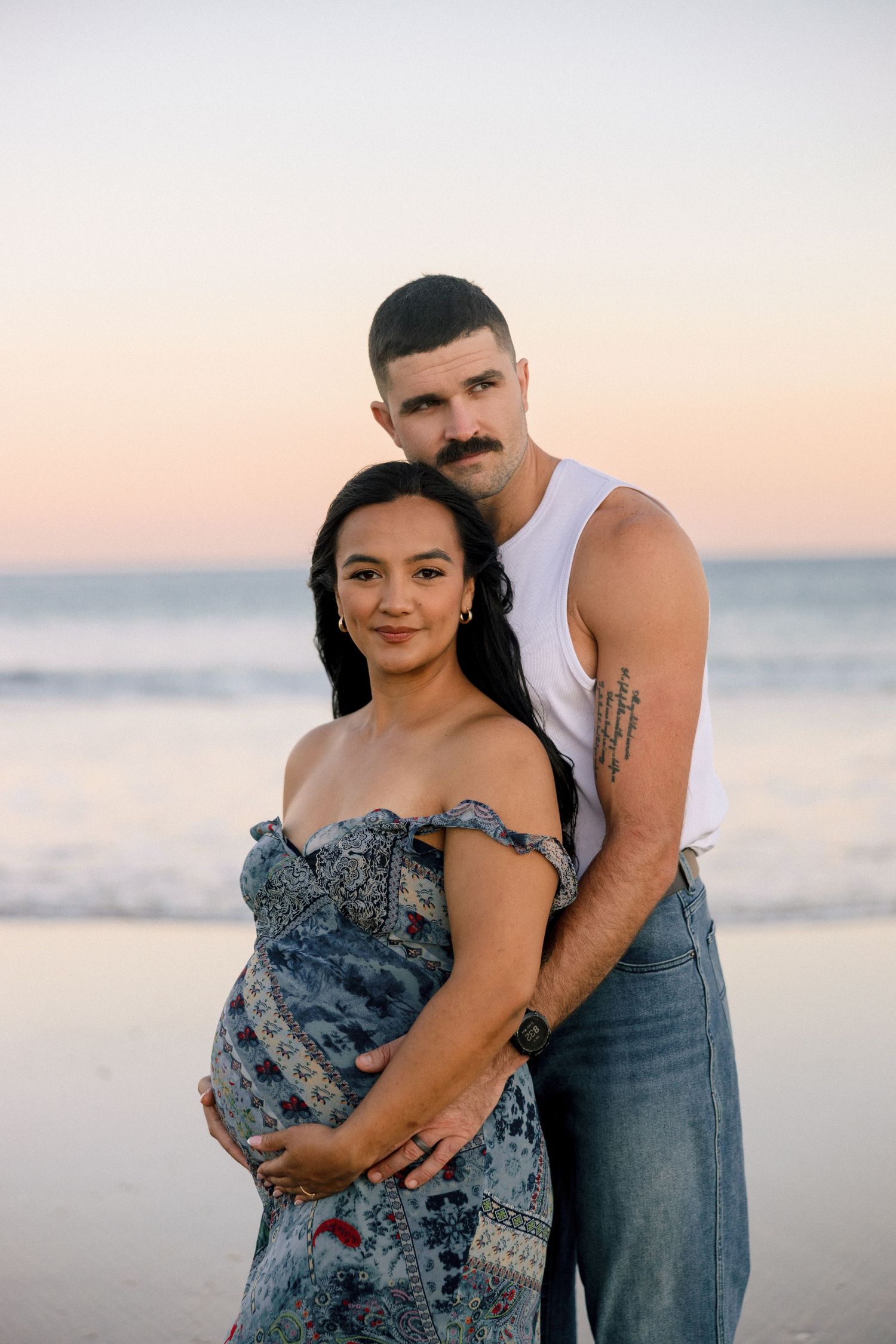 A romantic beach photoshoot at sunset featuring a couple embracing in coordinated blue and denim outfits.