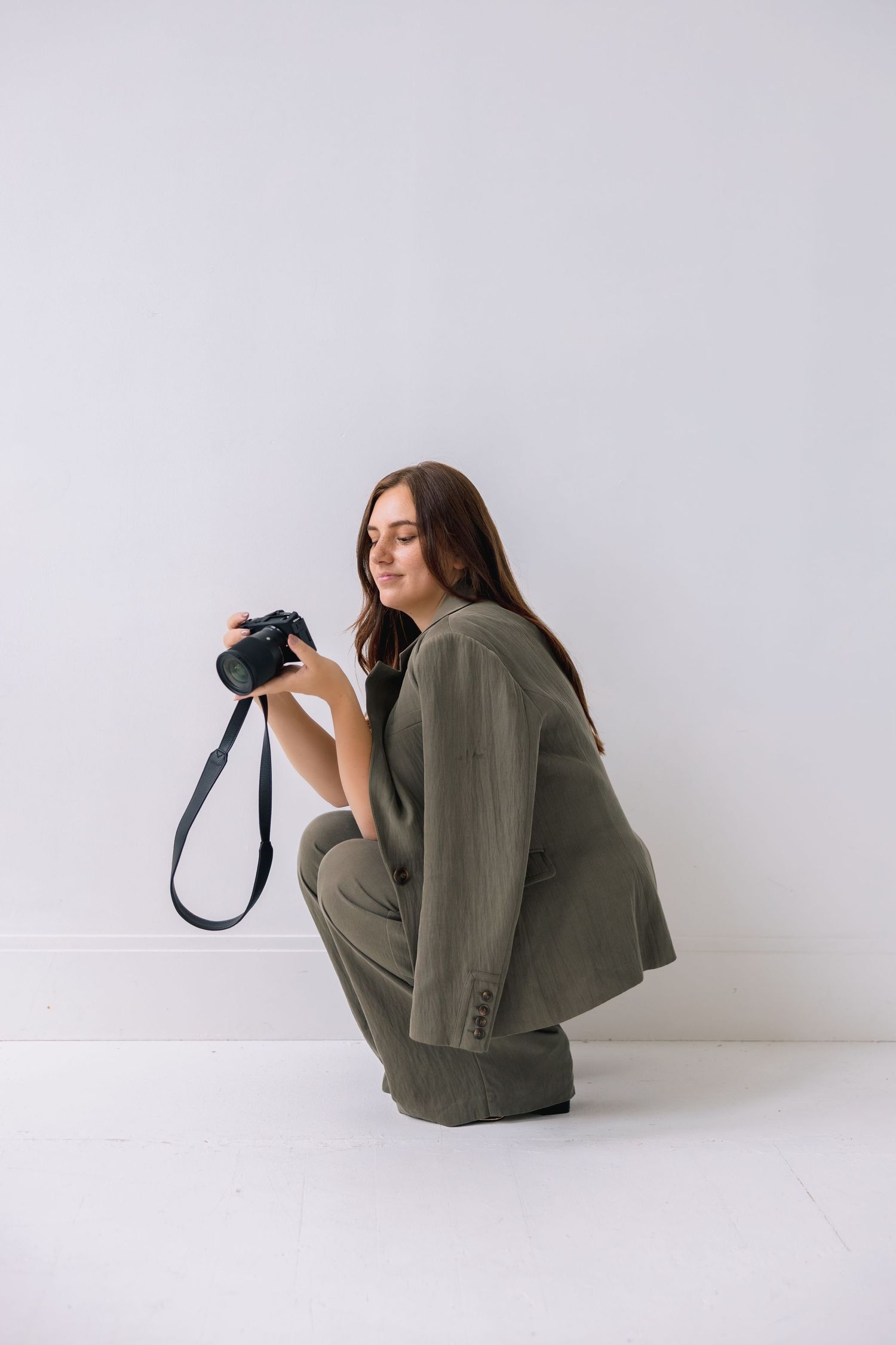 Artistic fashion photo series showing person in olive blazer curled up against white background in minimalist style.