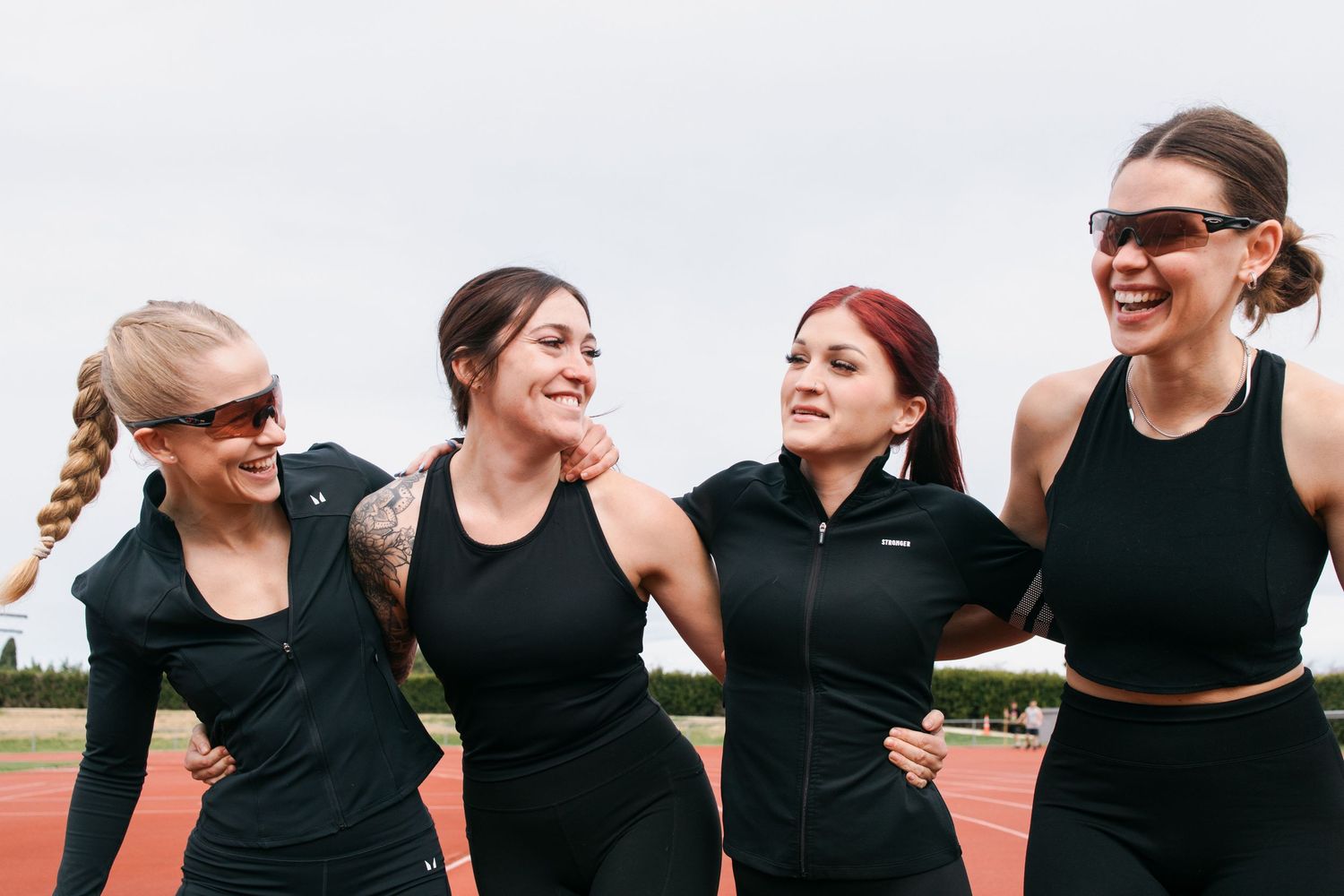 Four friends in athletic wear laughing together on a track during an outdoor workout session.