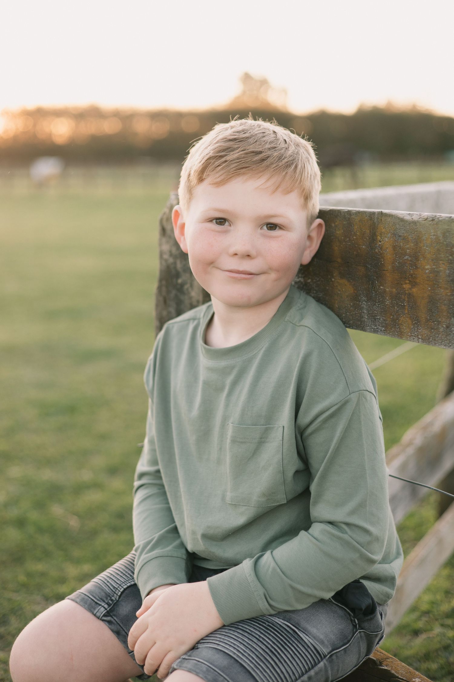 A casual outdoor portrait against a rustic wooden fence at golden hour.
