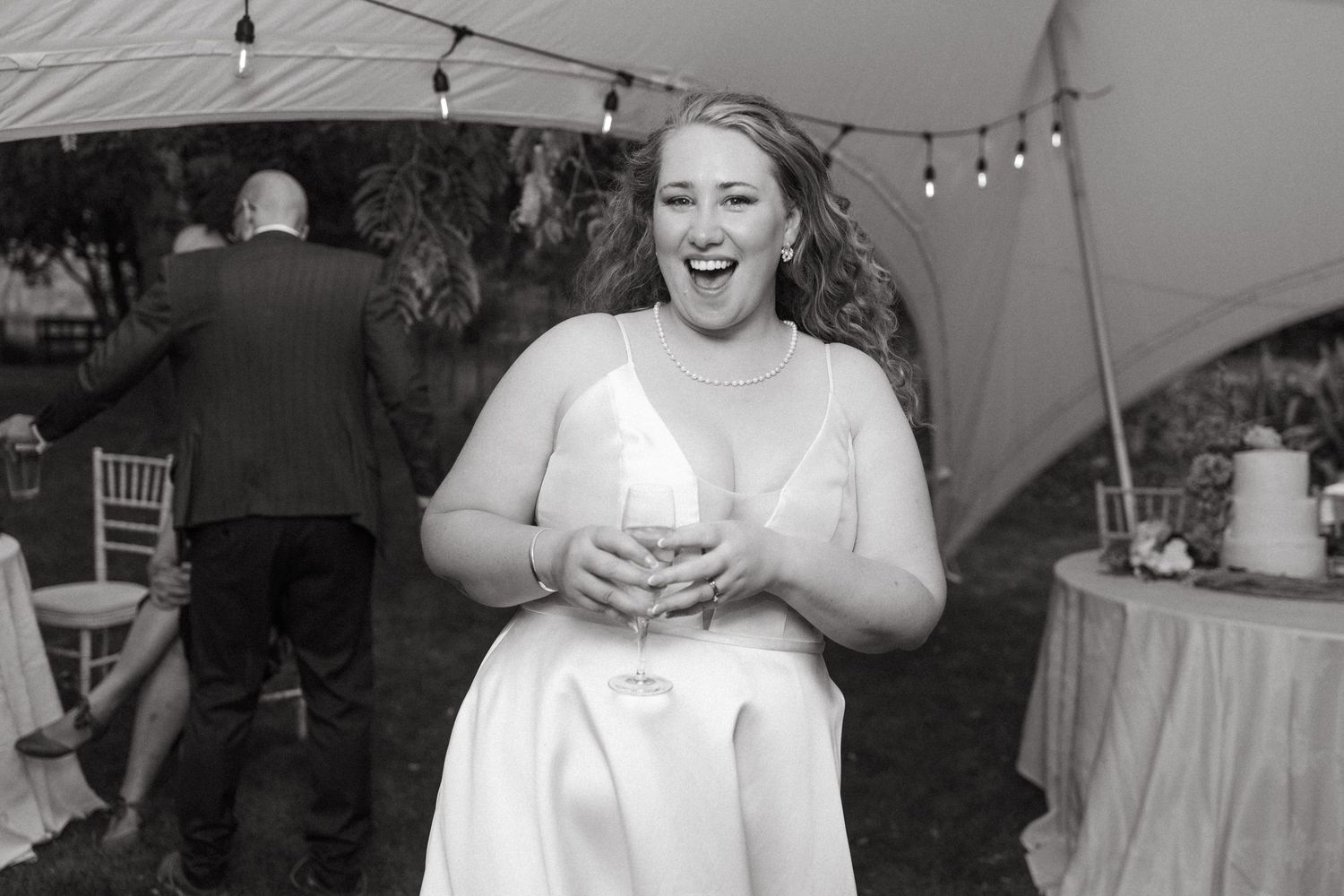 Joyful candid moment under string lights at outdoor wedding reception.