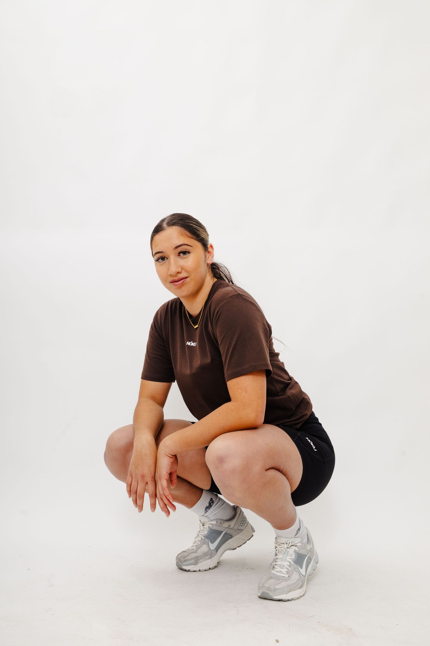 Model in athletic wear demonstrates squatting pose while wearing silver sneakers on white background.