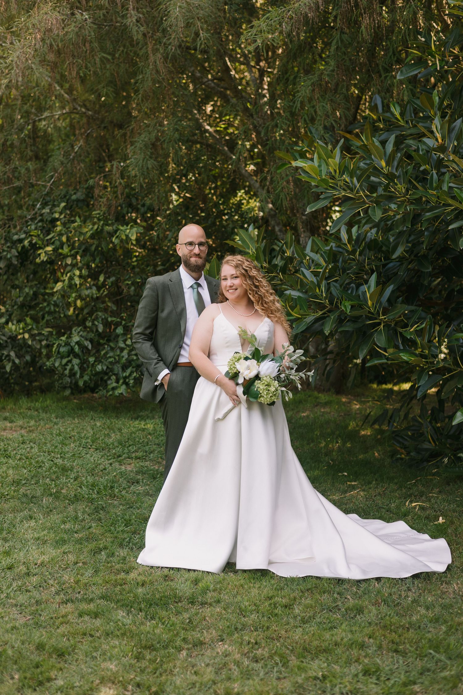 A couple poses together in a garden setting on their wedding day with the bride wearing a flowing white gown.