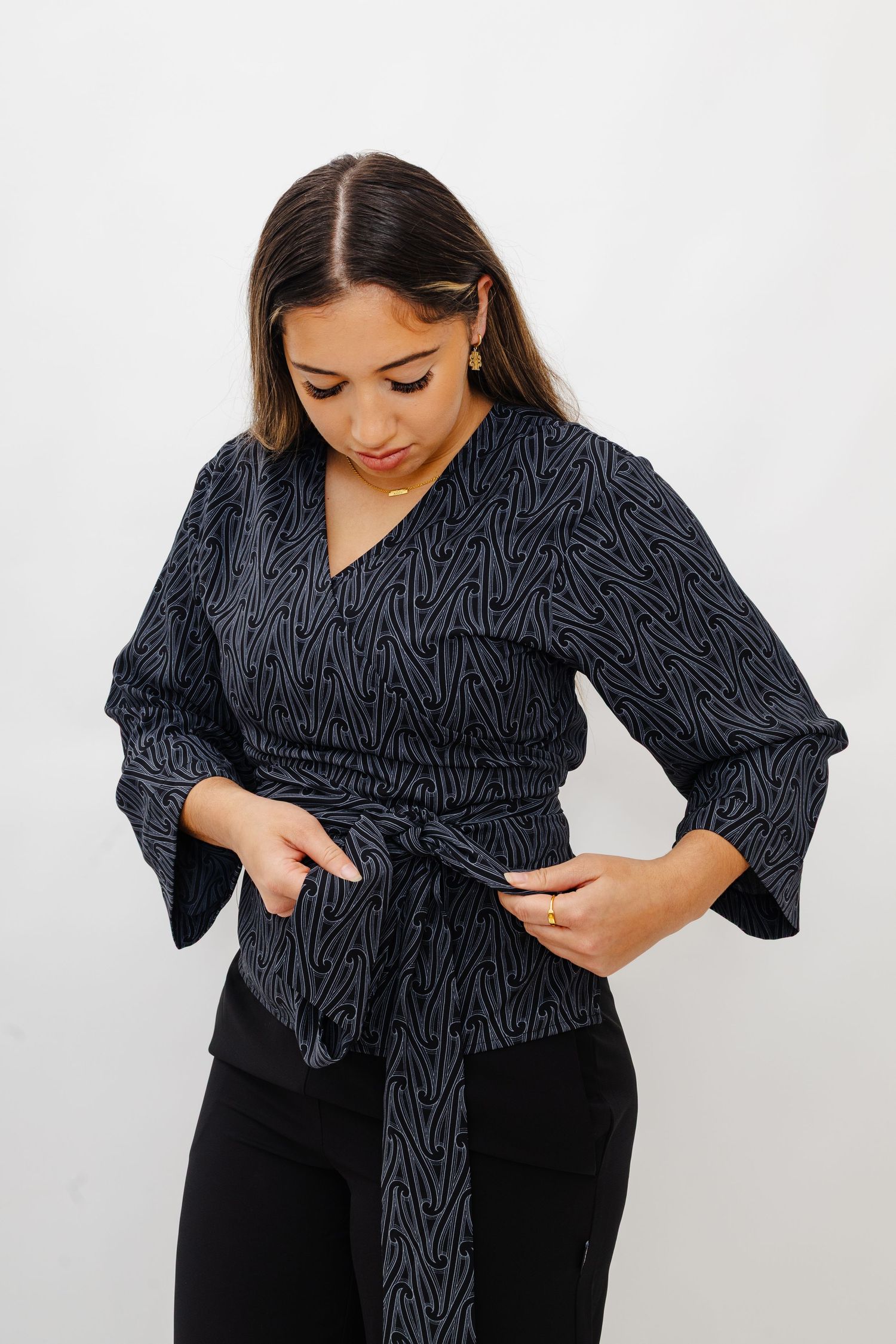 Woman in black and white patterned wrap top and black pants shown in multiple poses against white background.