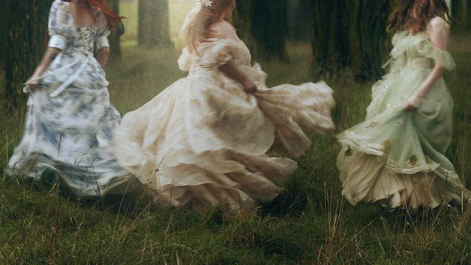 Three people in flowing vintage dresses twirl through a misty garden creating an ethereal, dreamy scene.