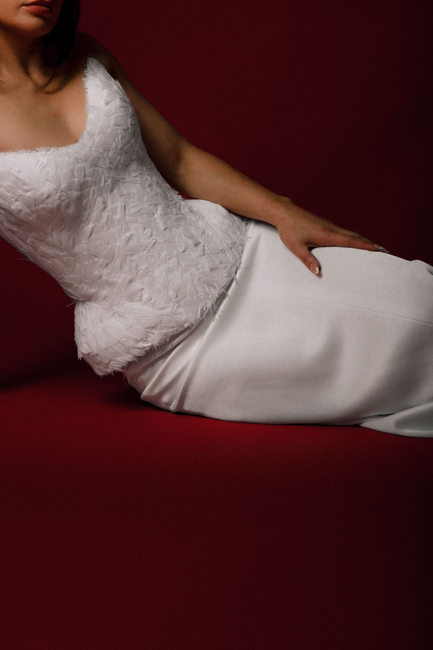 Woman in elegant white lace and satin wedding gown posed against a deep red background.