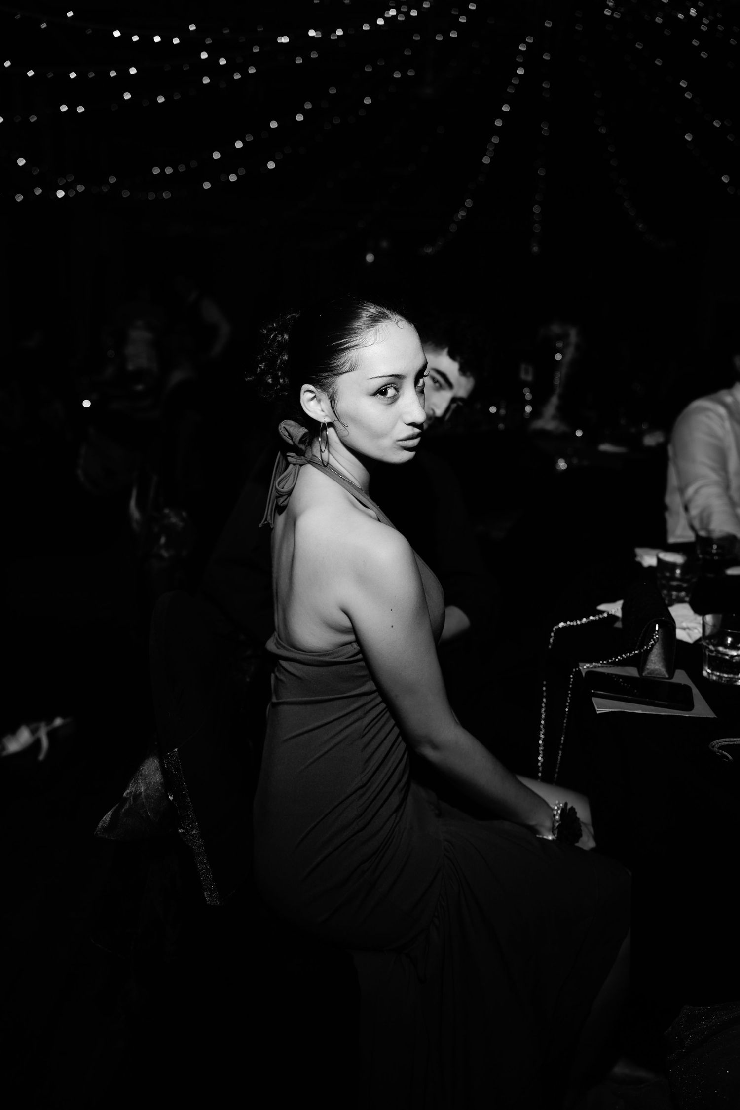 Black and white photo of a woman in a backless dress at an elegant evening event with string lights.