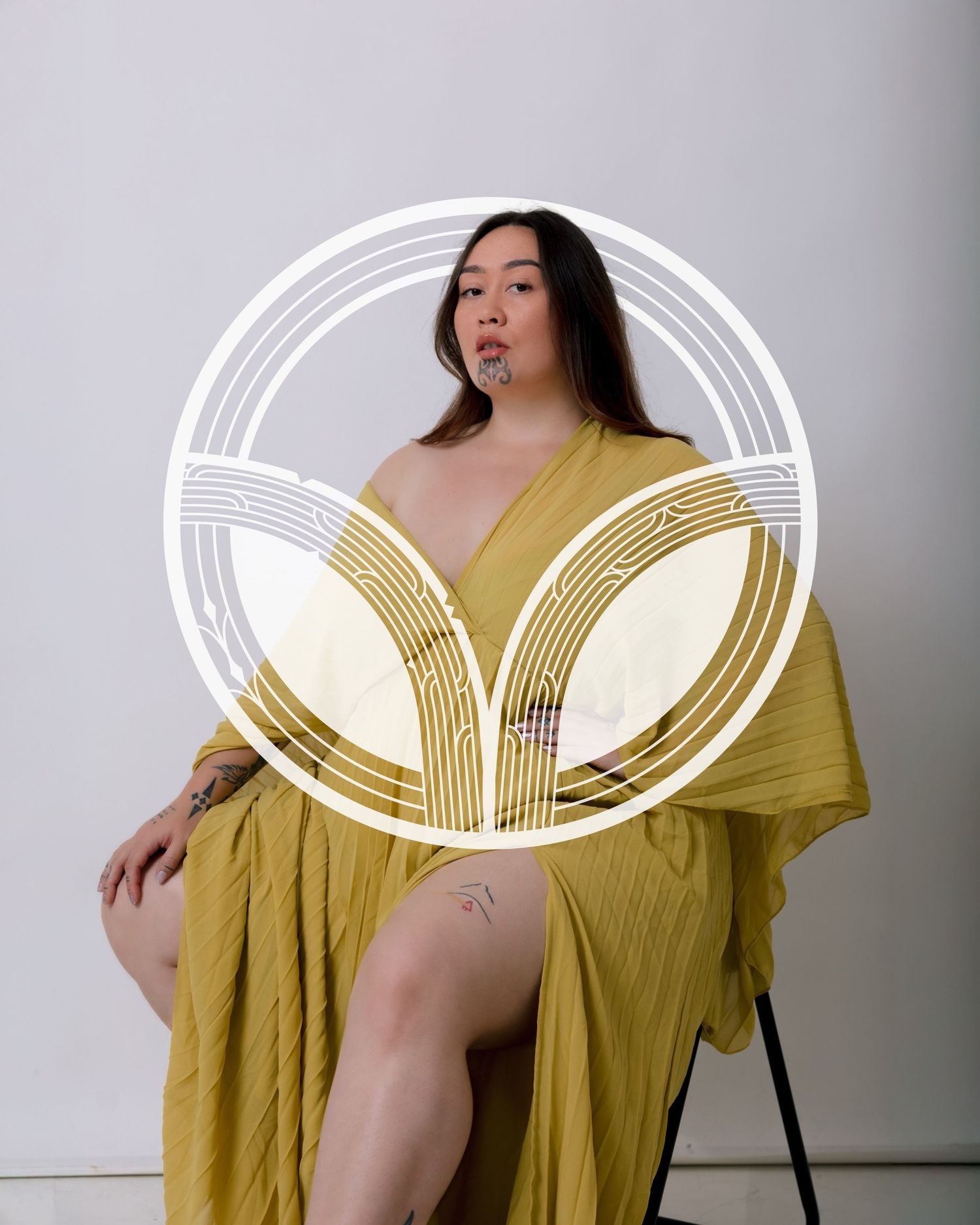 A figure draped in a flowing mustard yellow fabric poses artistically against a white backdrop.