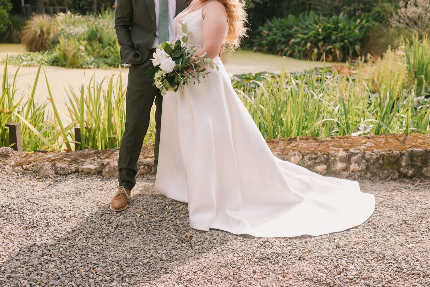 Elegant wedding dress flowing in outdoor garden setting with lush greenery.