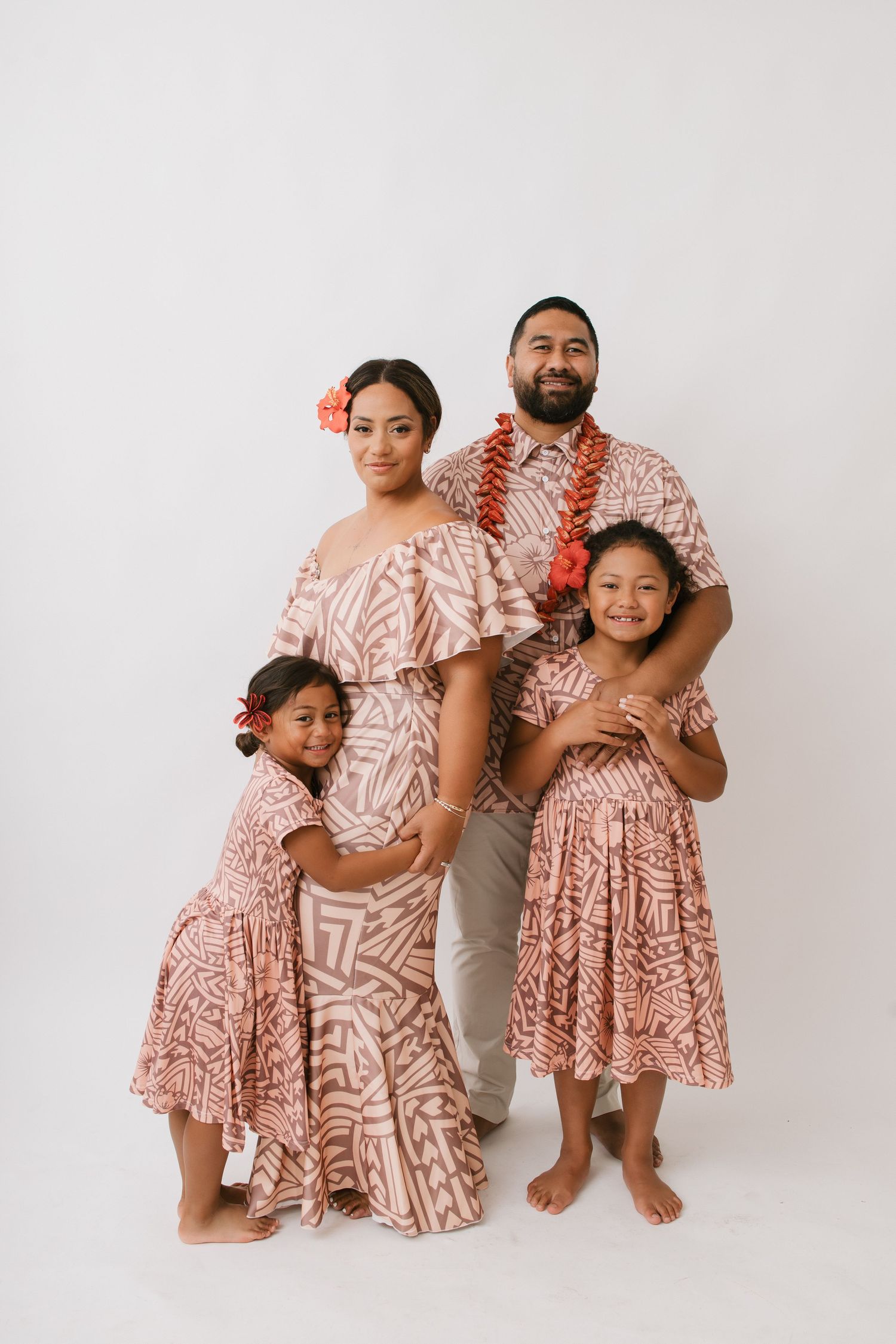 Family wearing coordinated pink and white tropical print outfits poses together against white background.