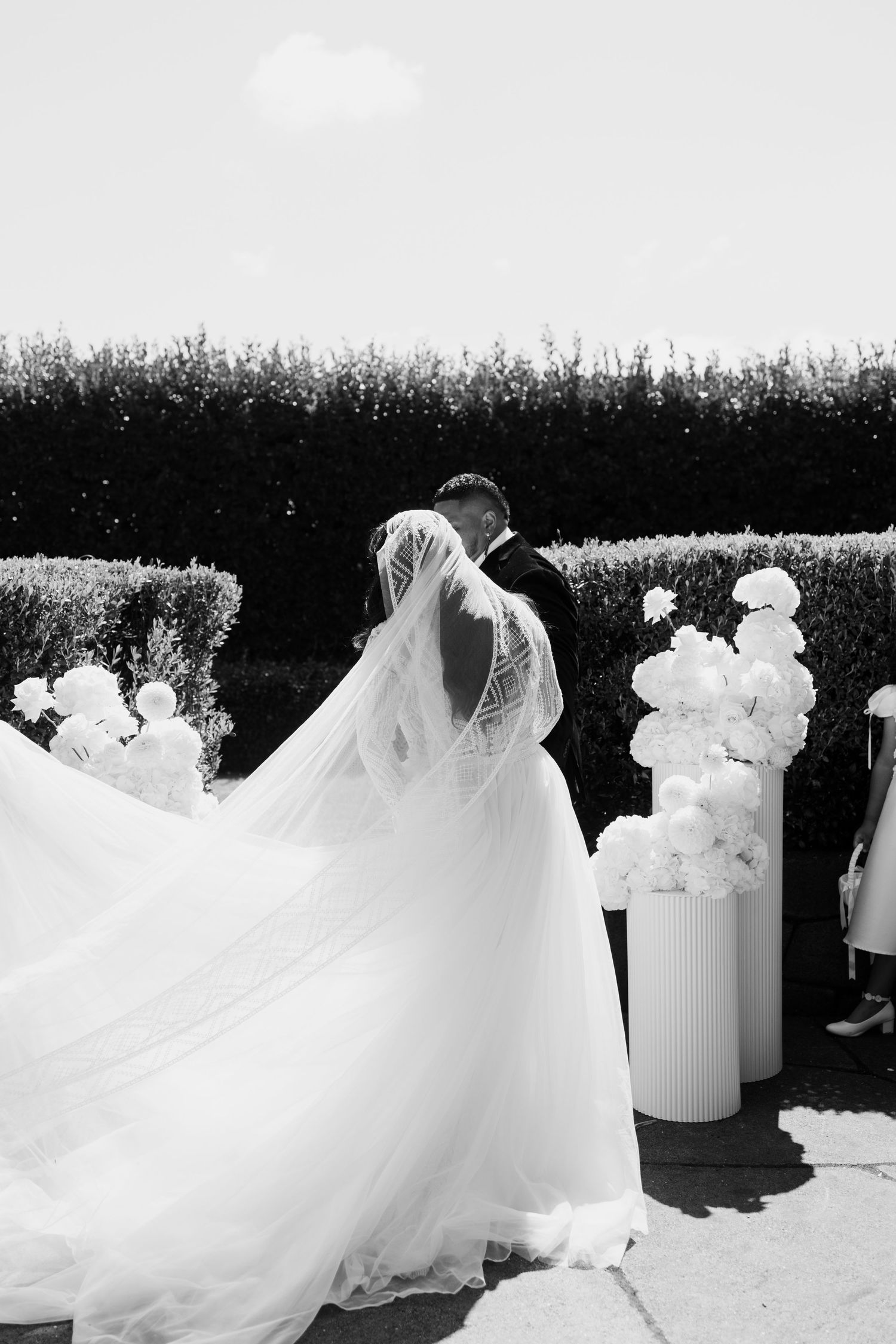 A wedding dress with flowing white tulle fabric creates an ethereal silhouette against a natural outdoor backdrop.