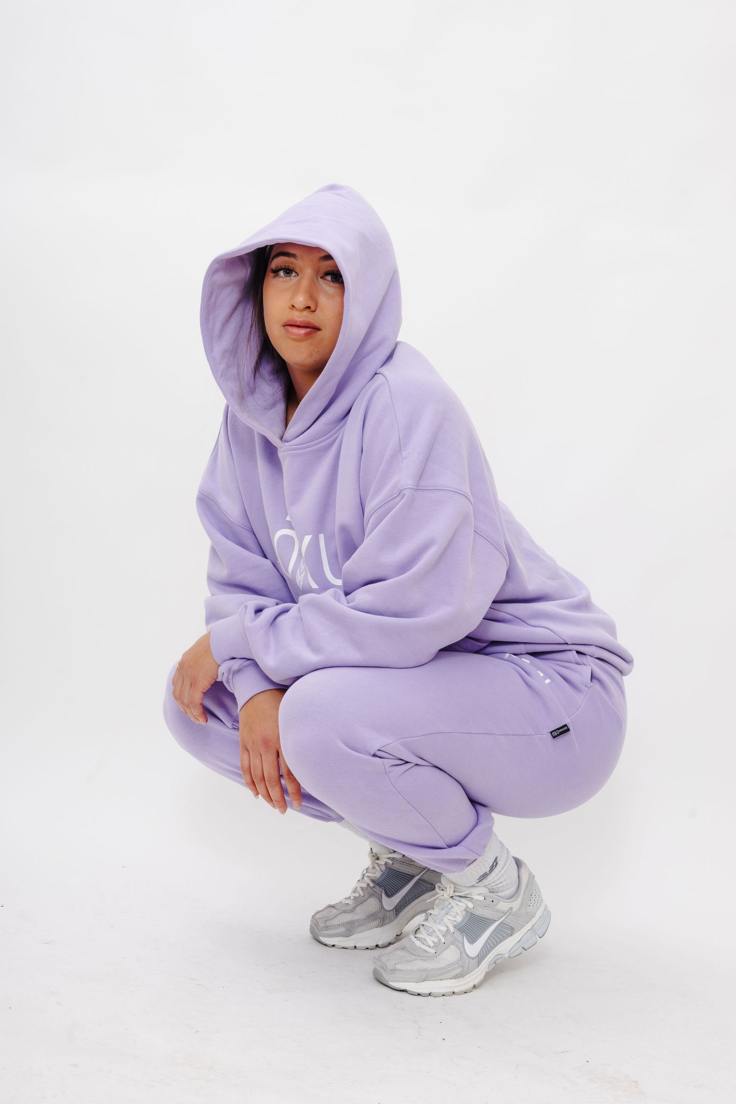 Person wearing lavender hoodie and sweatpants crouching in different poses against white background with gray sneakers.