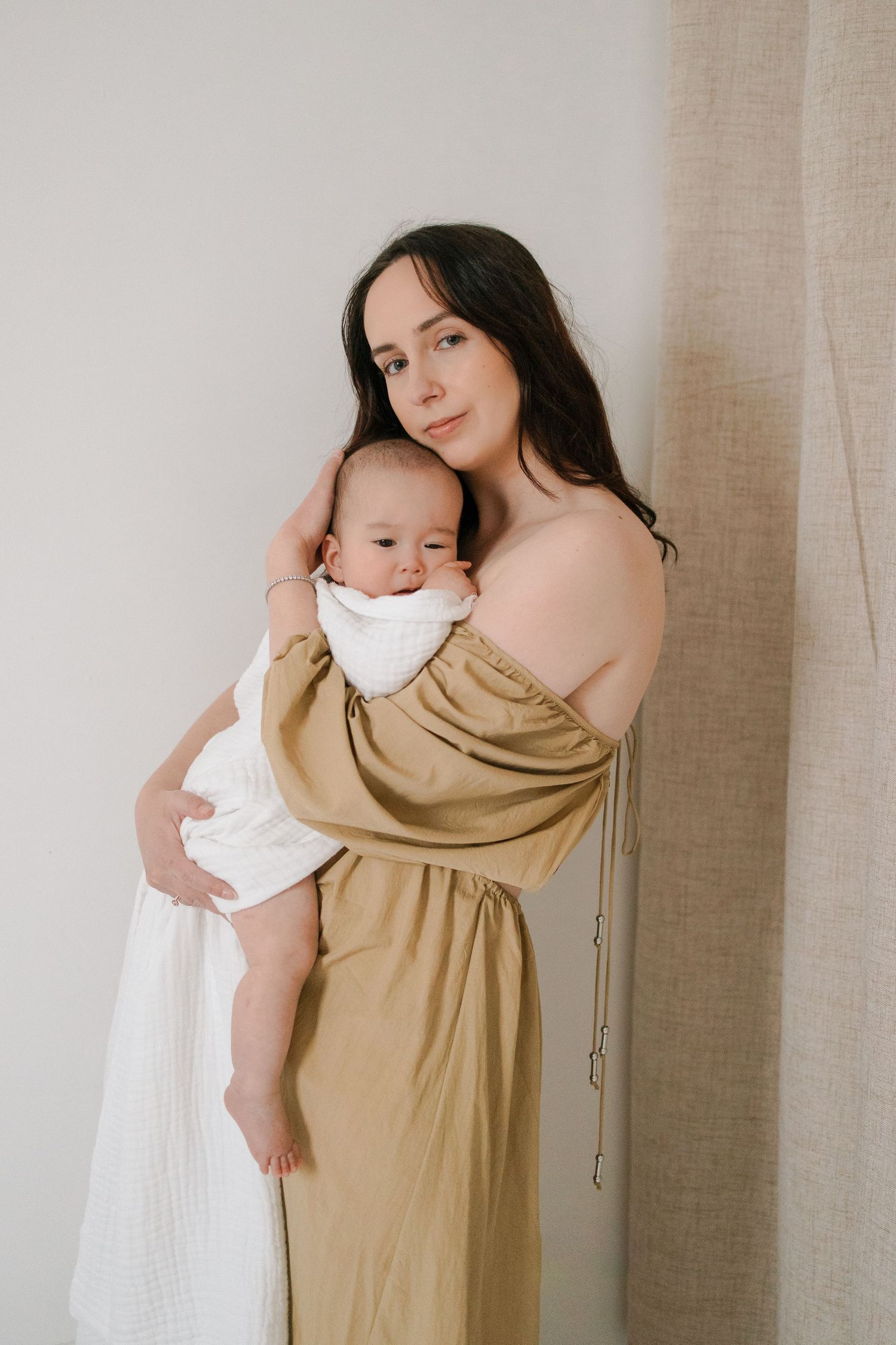 A tender moment captured in soft beige tones as a parent embraces a baby wrapped in white against a neutral background.