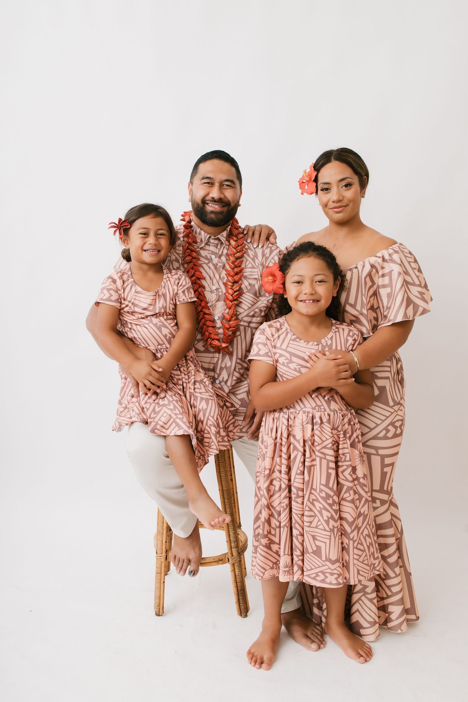 Family wearing matching pink and white floral outfits poses together on white background in studio setting.