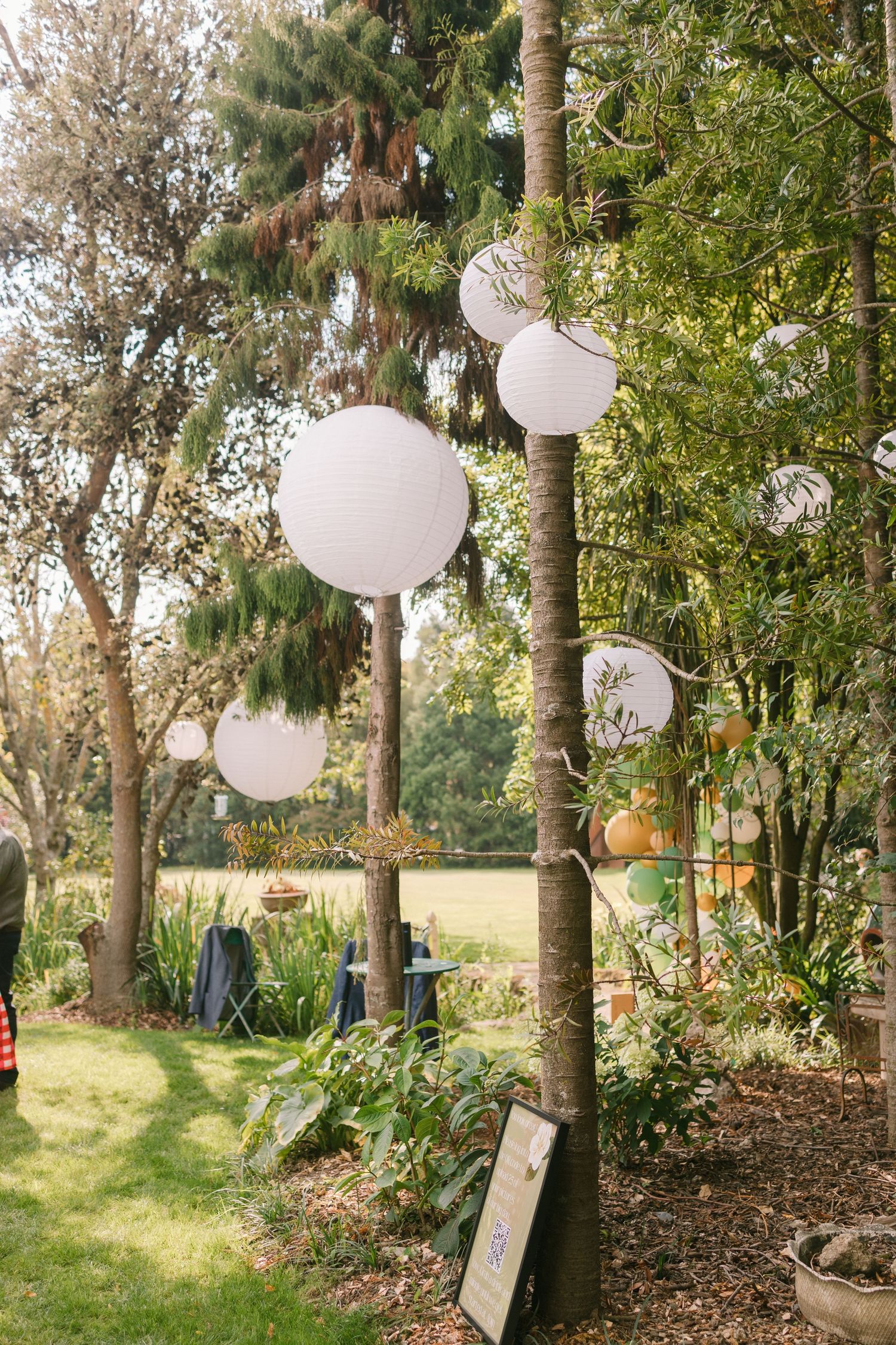 White paper lanterns hang from trees at an outdoor garden wedding reception.