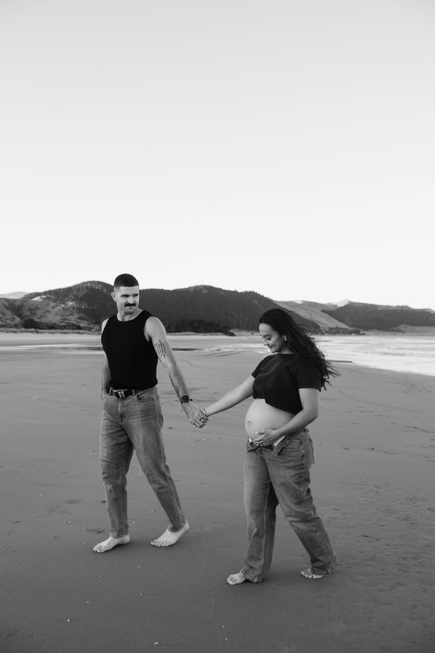Playful couple holding hands and dancing together on an empty beach in black and white.