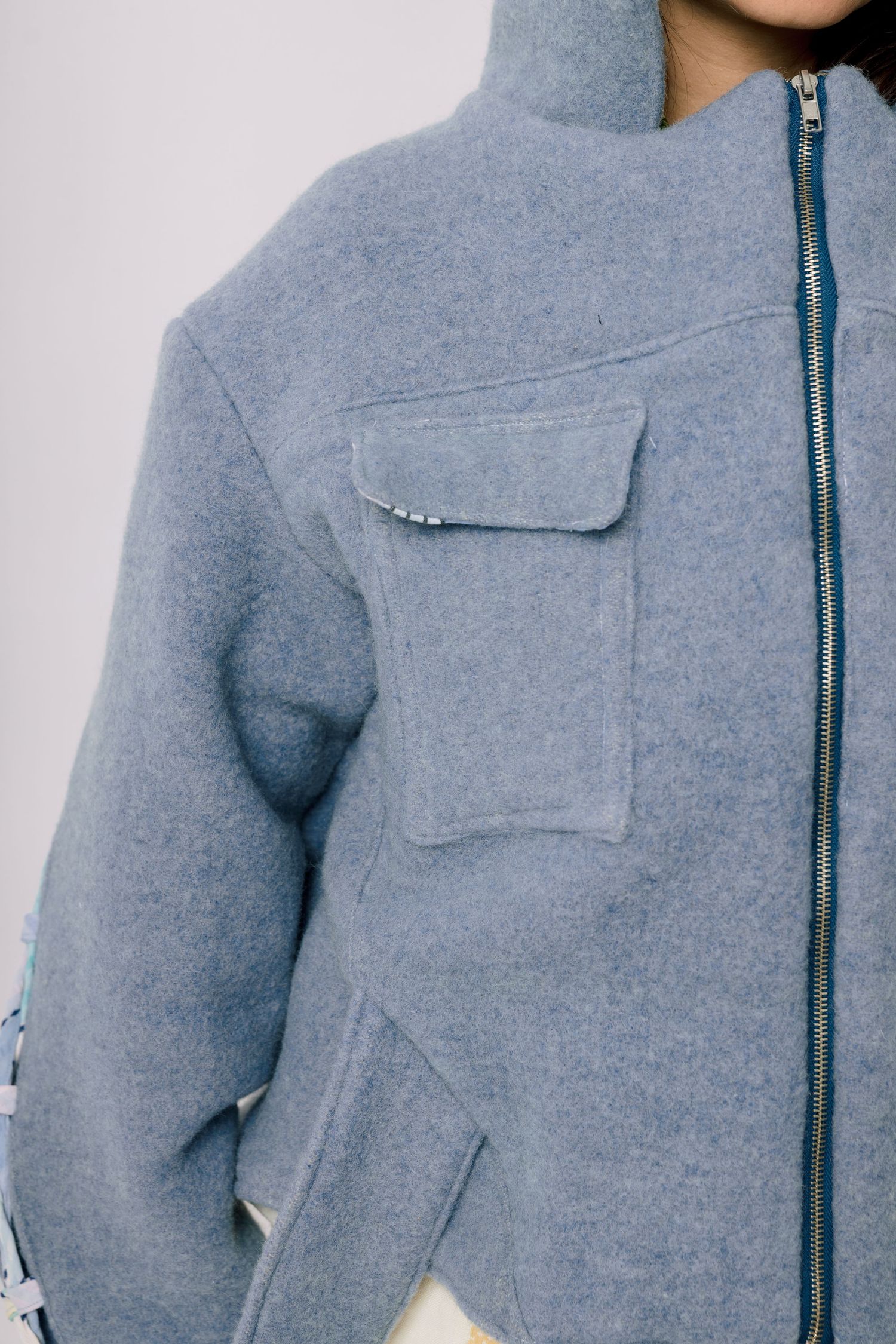 Close-up detail of a gray wool zip-up jacket showing chest pocket and minimal design details.