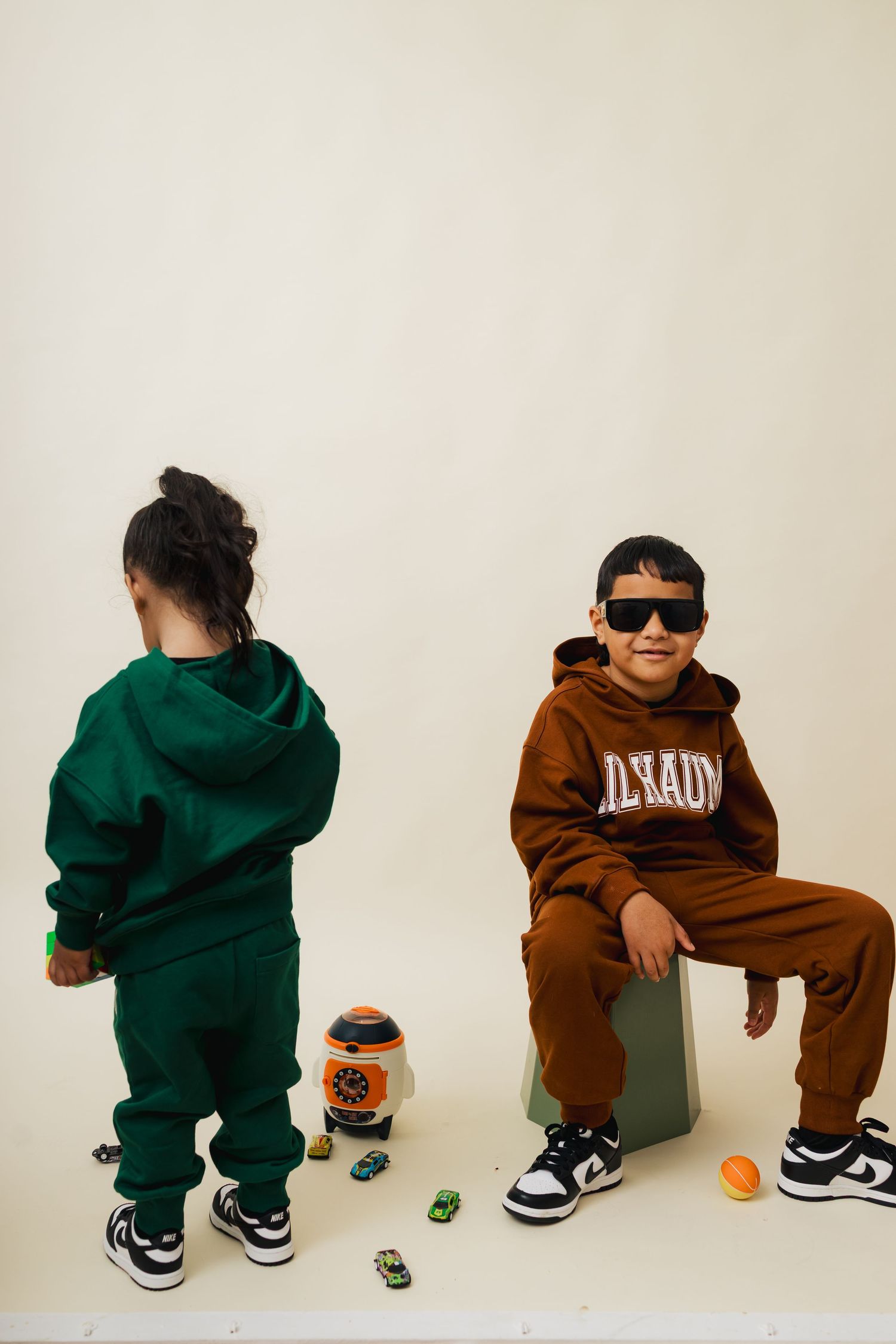 A series of photos showing a toddler in alternating green and brown outfits sitting on the floor with sneakers.
