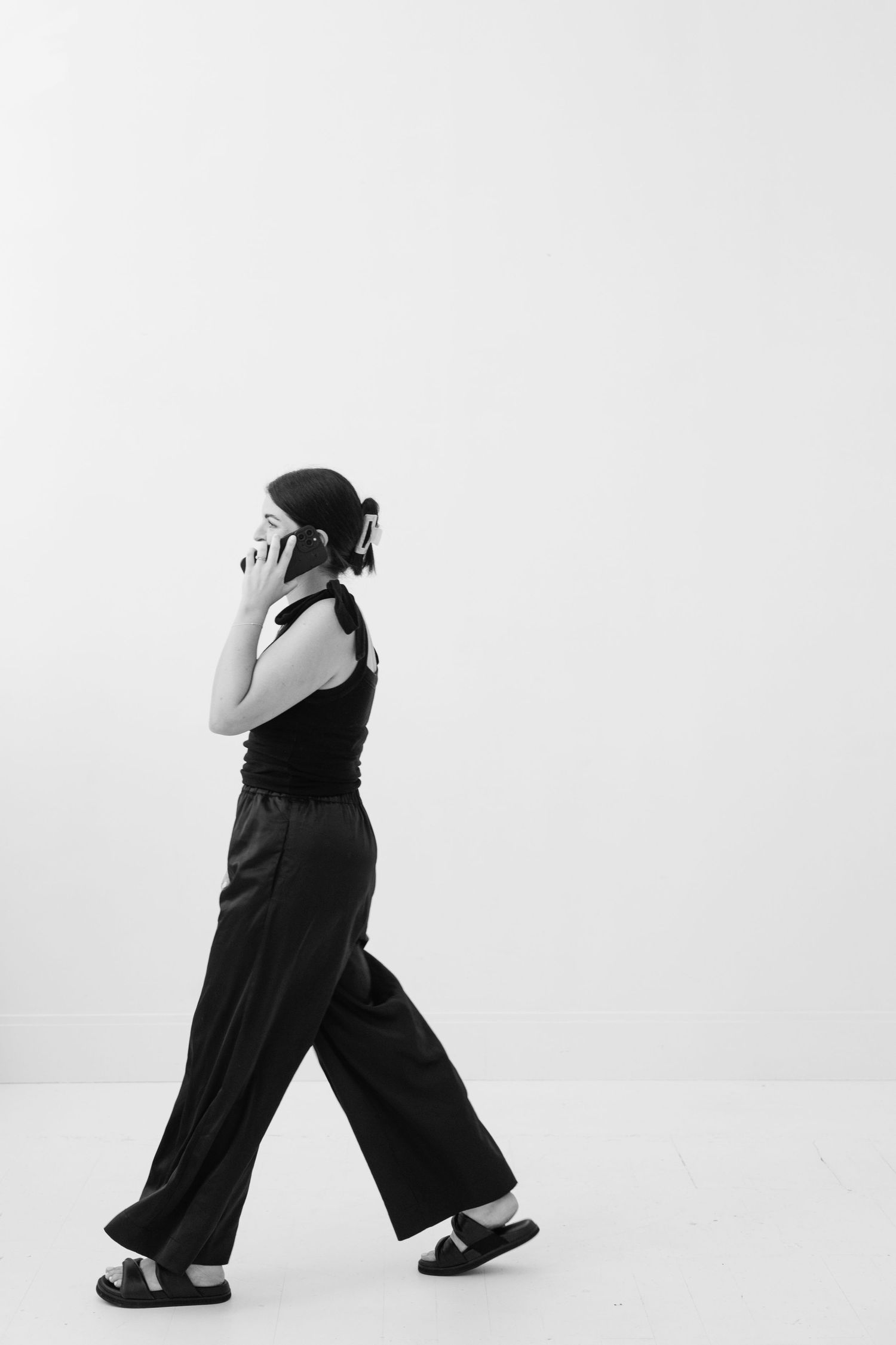 A person in black attire and beret walks sideways while holding their head in a minimalist black and white composition.