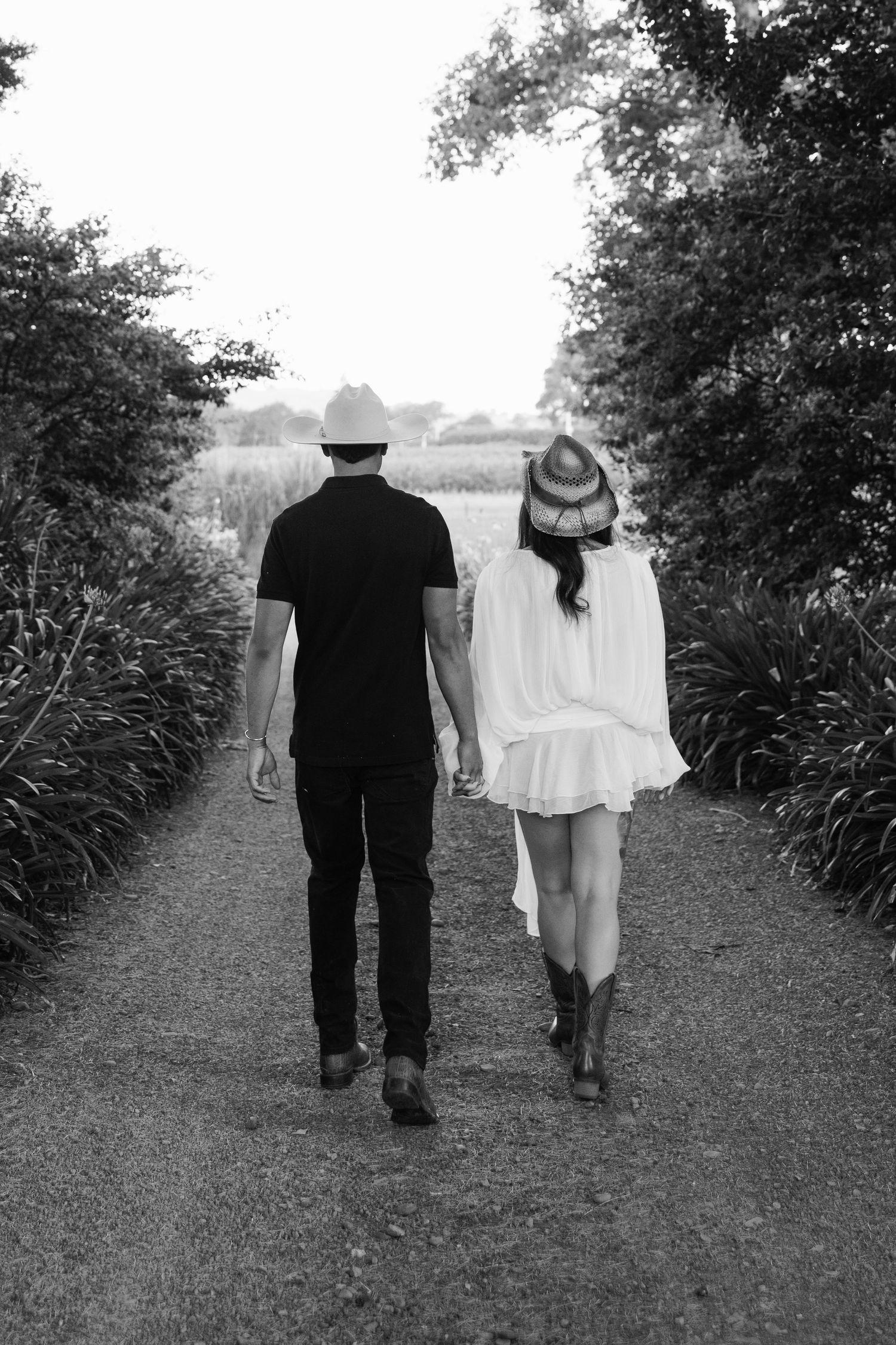 A black and white photo shows two figures walking down a tree-lined path together.