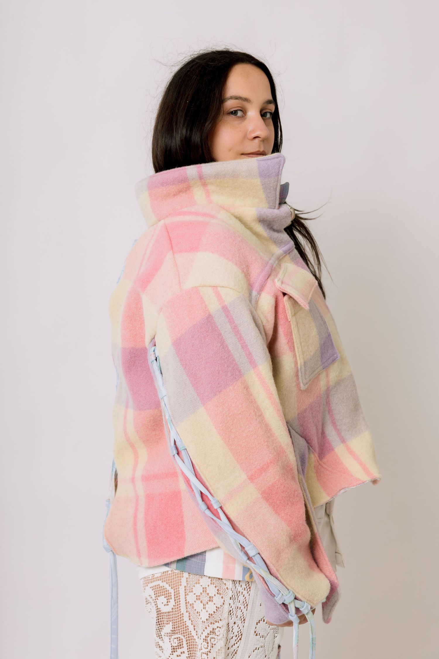 Model wearing pastel plaid jacket in pink and yellow tones poses against white background.
