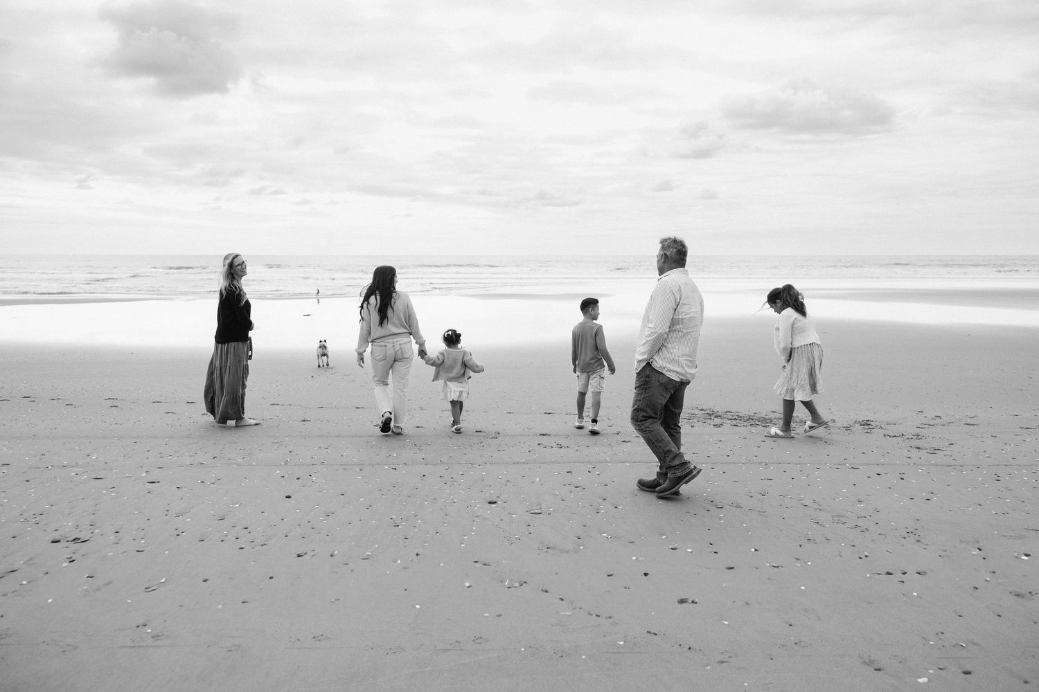 A sequence of black and white photos showing people walking and playing on a sandy beach near the ocean.