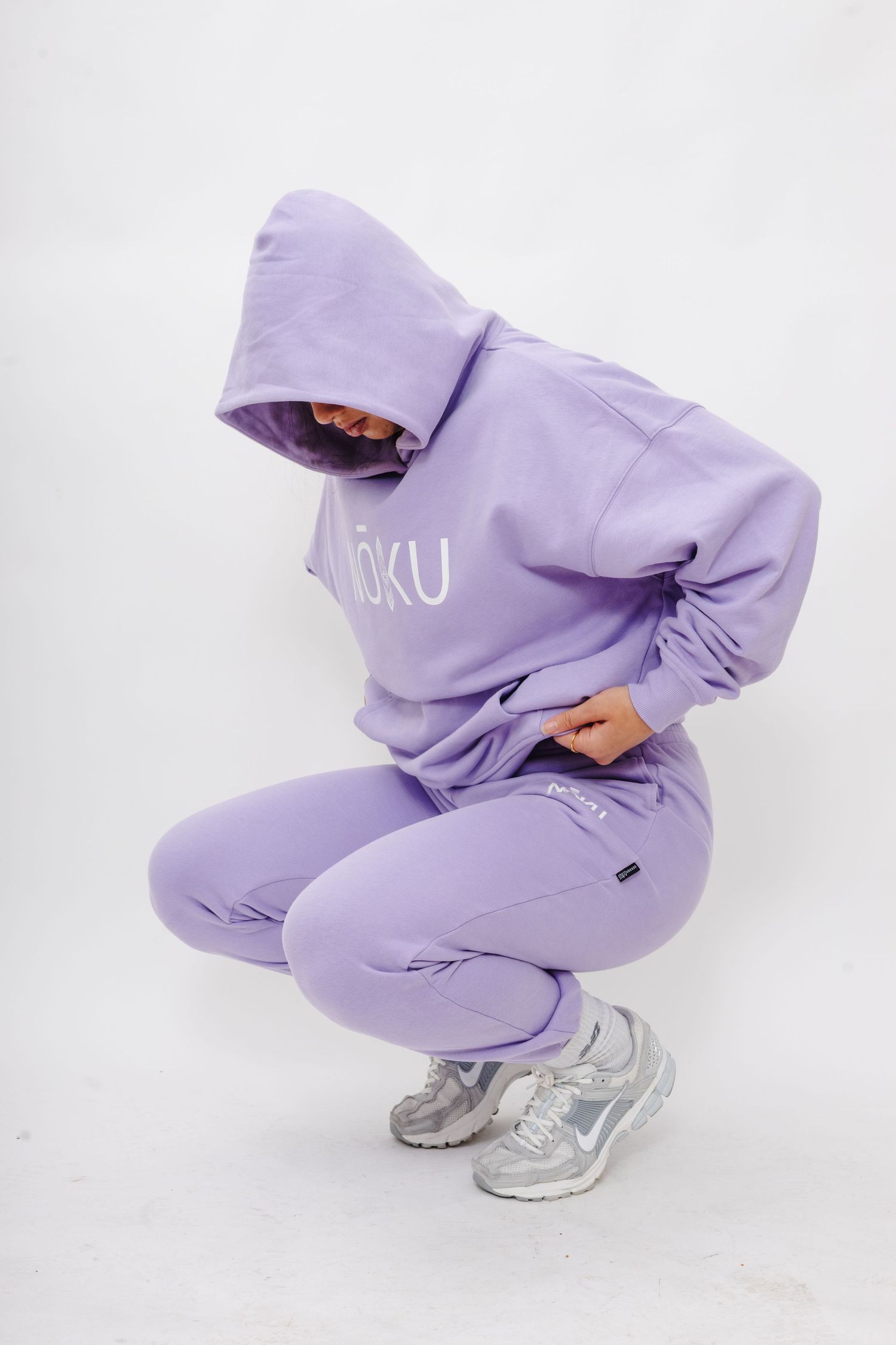 Person wearing a lavender sweatsuit and silver sneakers crouching in a dynamic pose against a white backdrop.