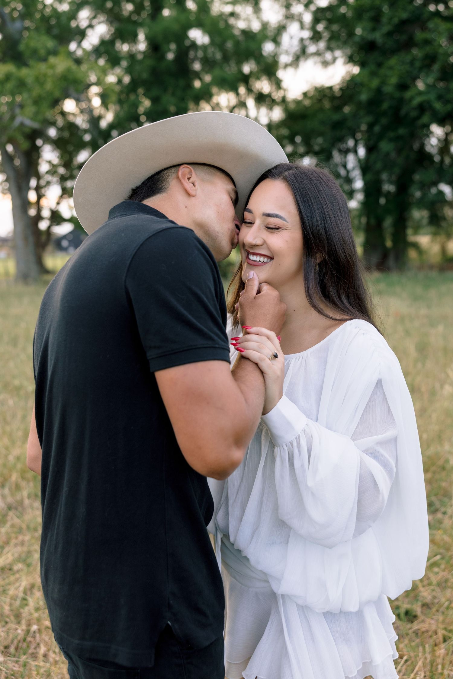 A romantic moment between a couple in contrasting black and white outfits standing in a sunlit meadow.