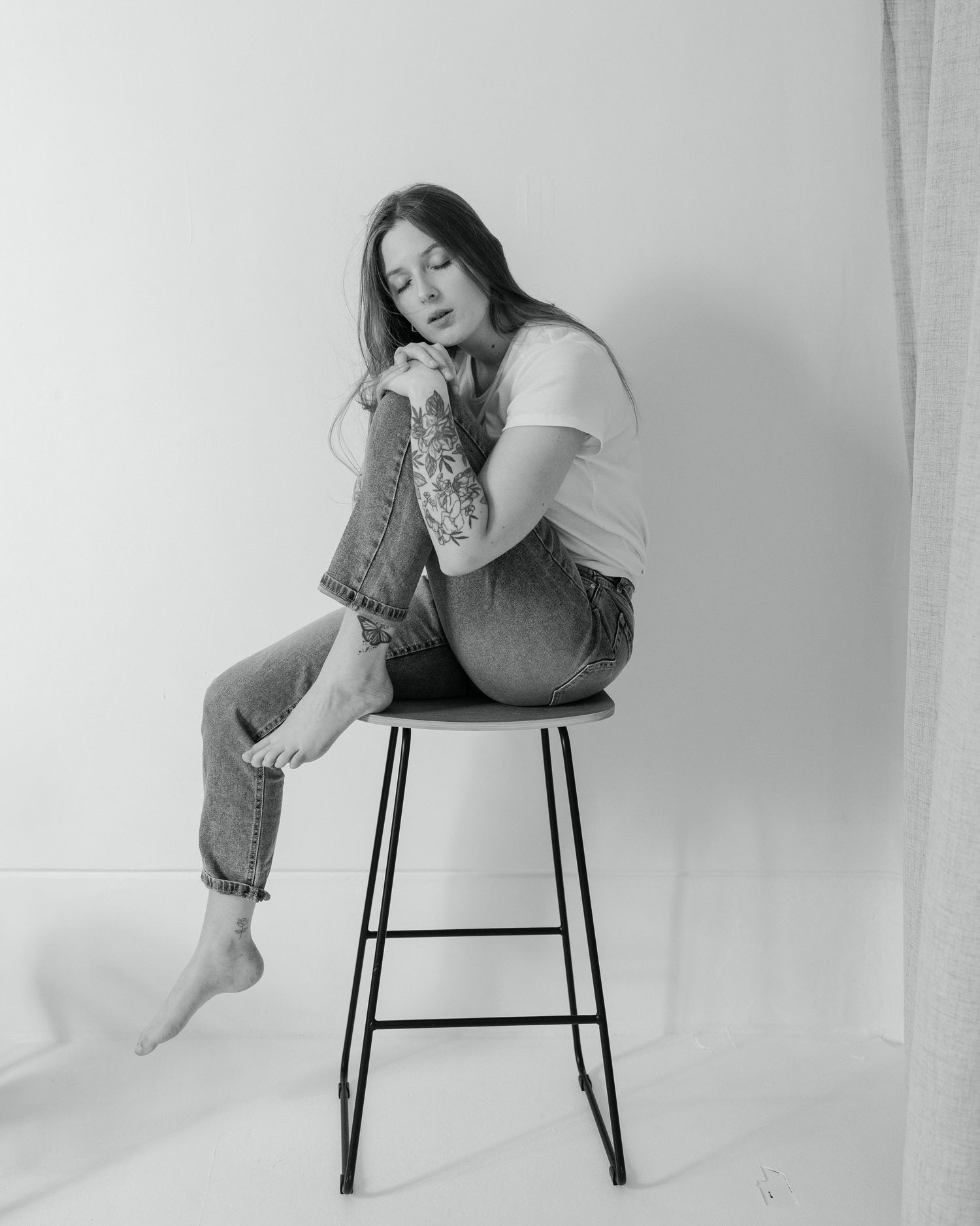 Black and white artistic photo series showing a person in casual attire posing on a modern chair against white backdrop.