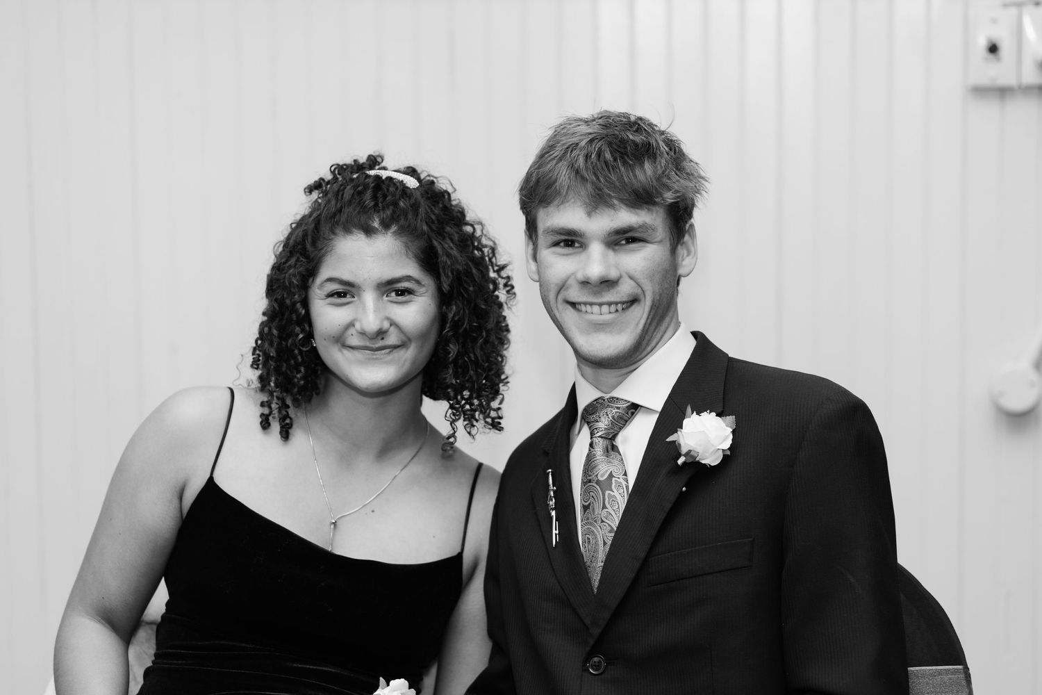 Black and white photo of a smiling young couple dressed formally, posing together at a prom or special event.
