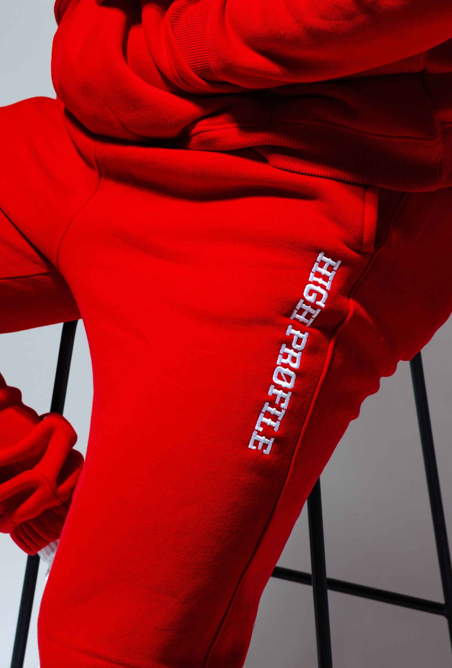 Close-up view of bright red sweatpants with white text branding on the leg against a gray background.
