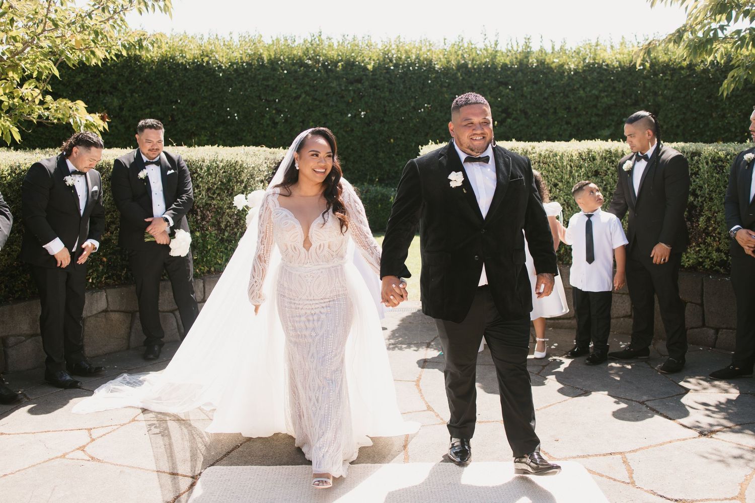 A joyful wedding celebration with the couple leading a procession on a stone patio.