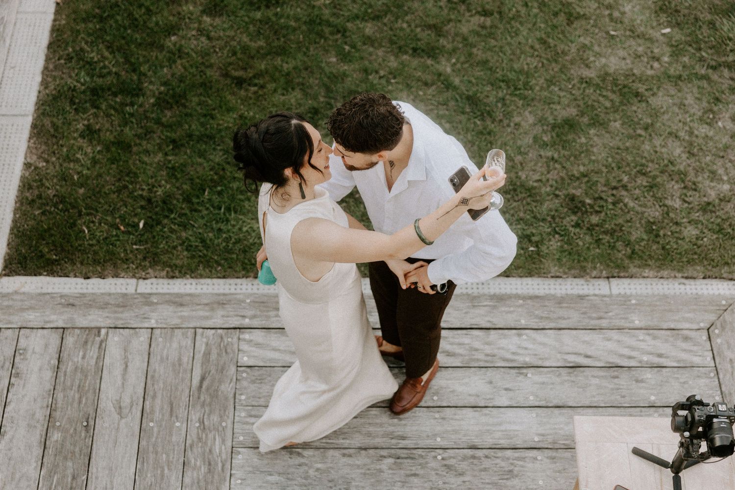 Aerial view of two people dancing on a wooden deck surrounded by grass.