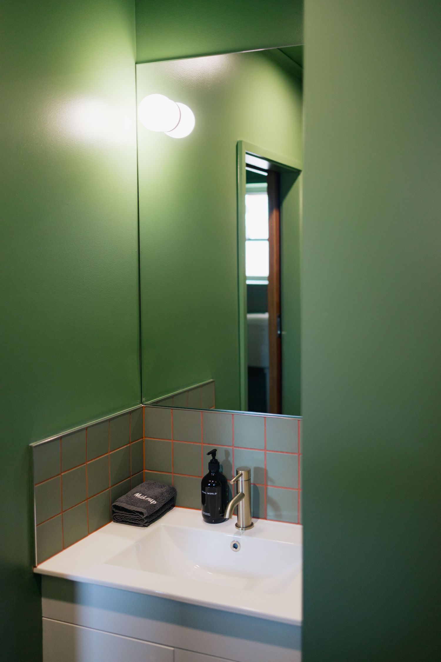 Modern bathroom vanity with white sink and green tiled walls.