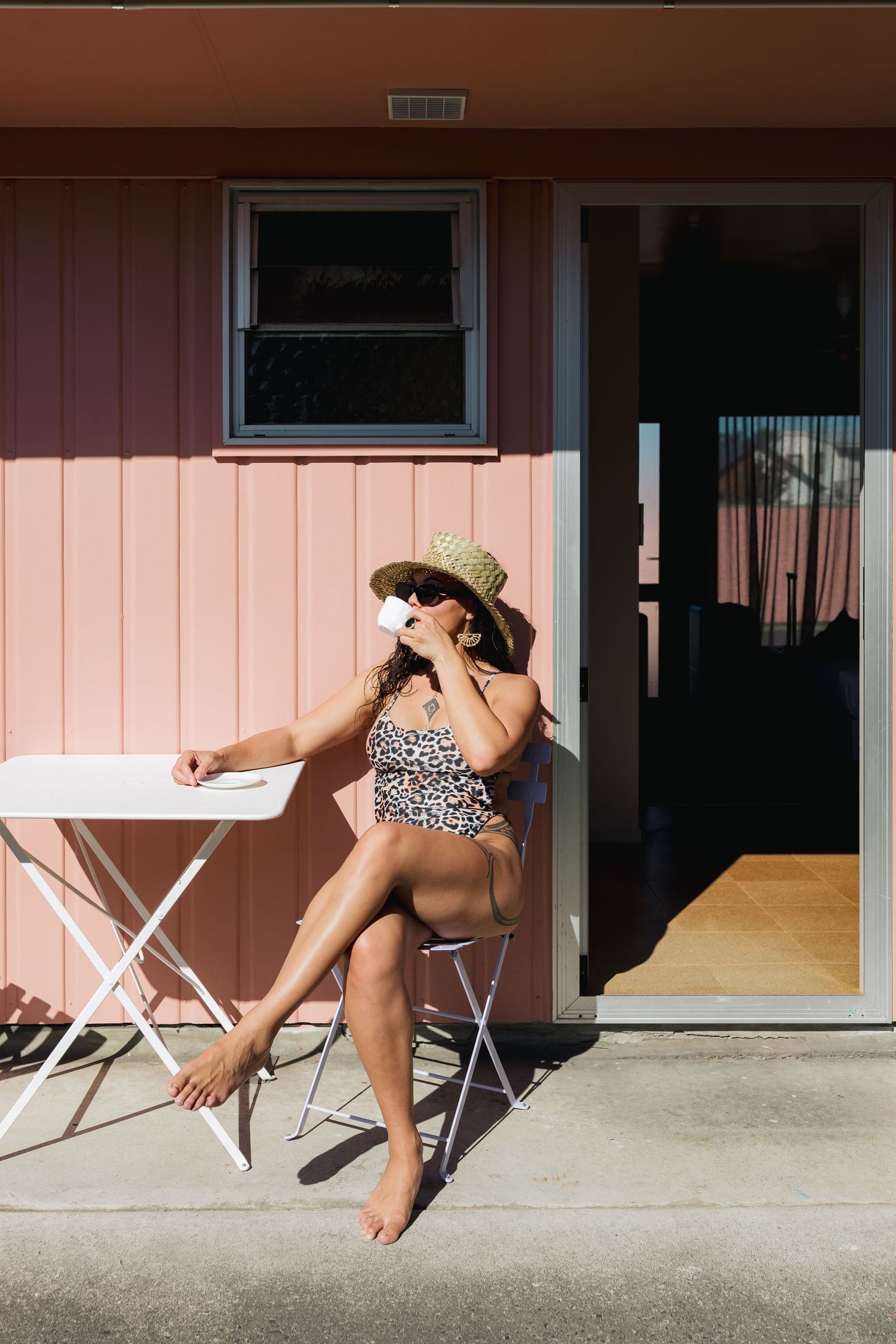 Guest lounging in a straw hat at a retro pink motel patio.
