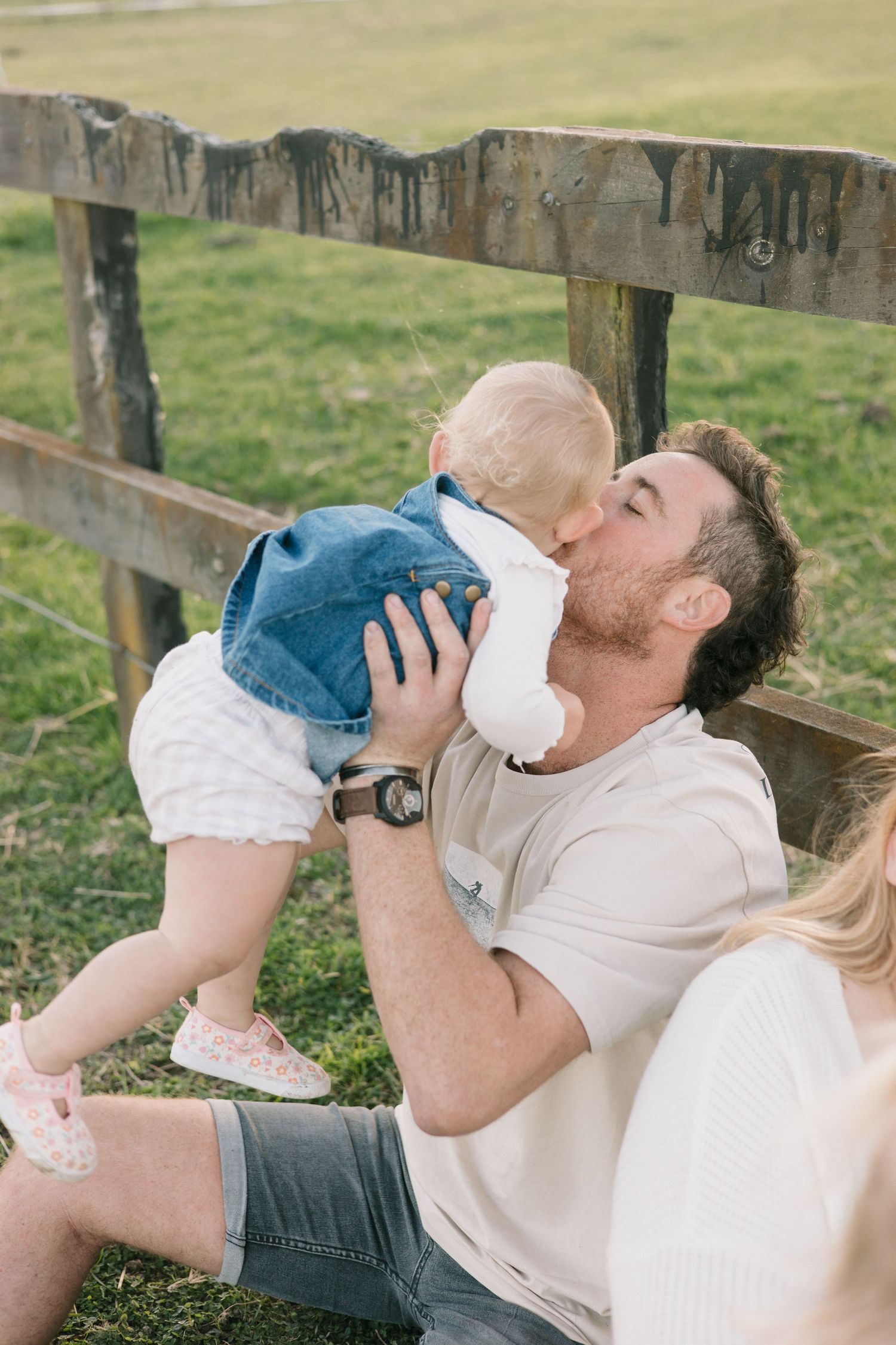 A heartwarming moment between parent and baby sitting on a wooden fence in a rural setting.