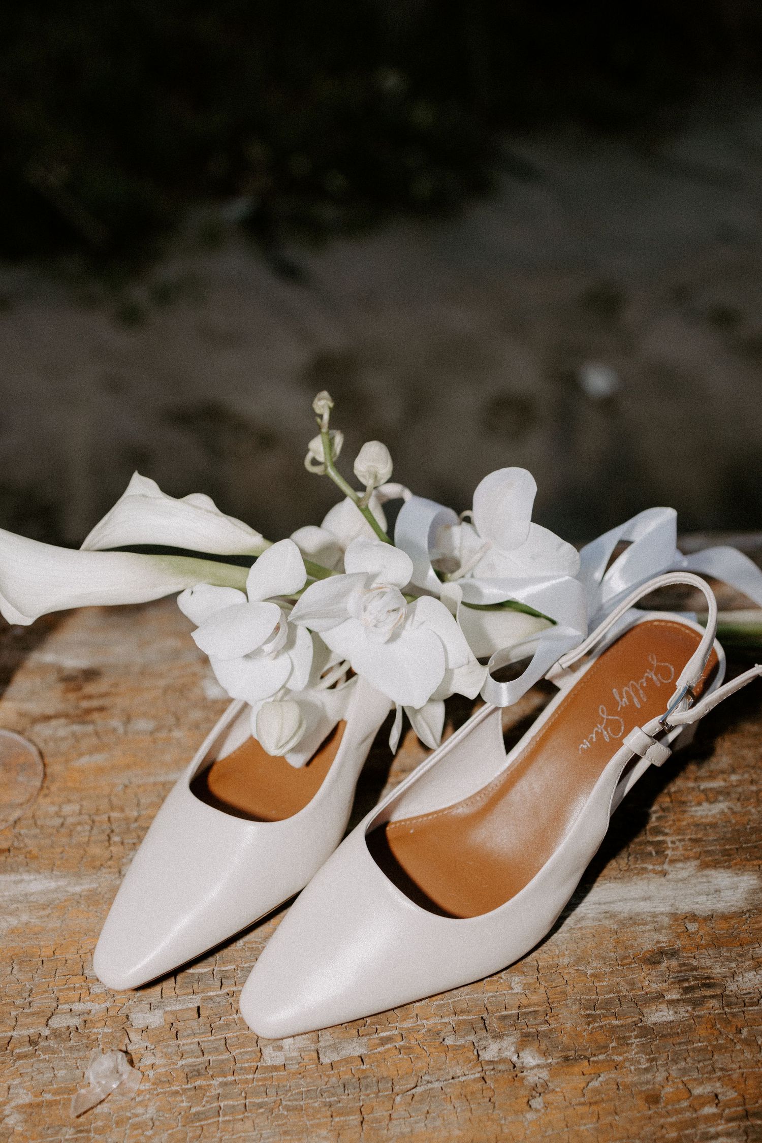 White bridal flats with floral details displayed on weathered wooden surface.