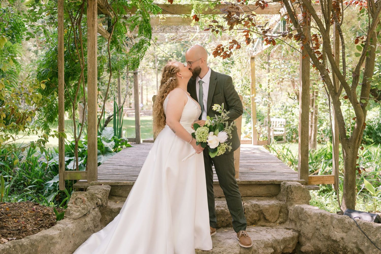 Couple posing under garden archway while holding floral wedding bouquet.