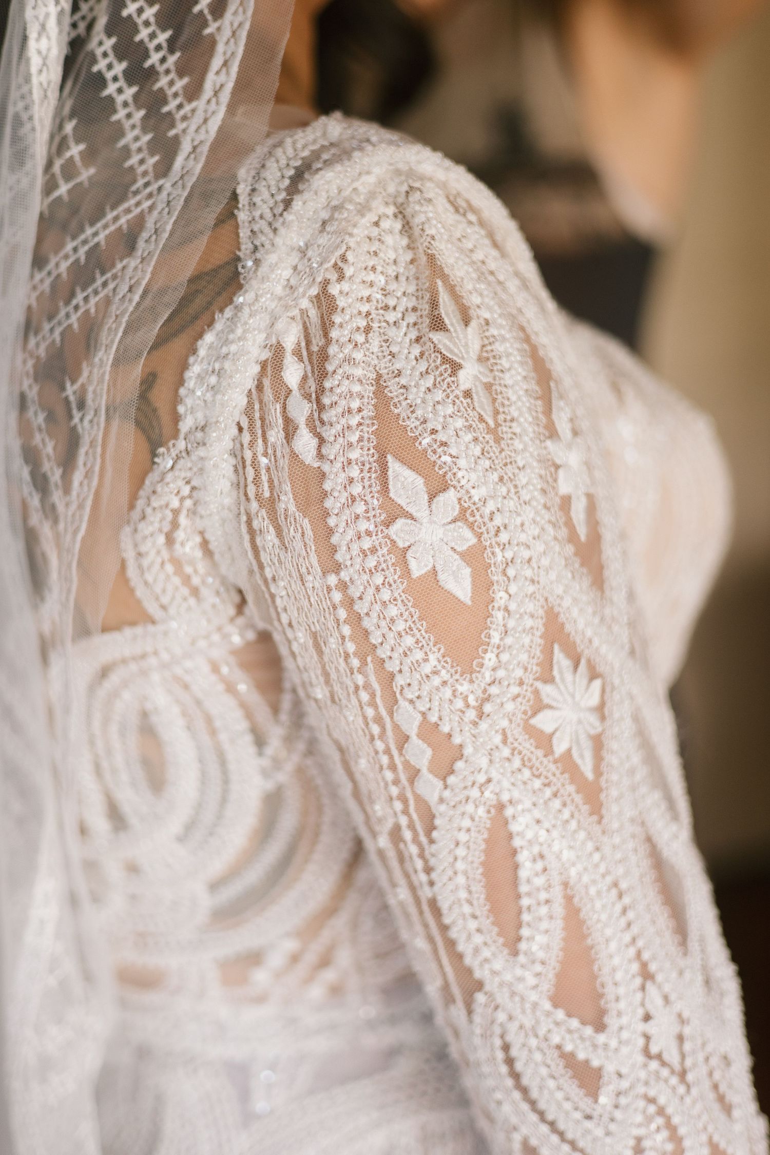 Intricate lace sleeve detail of a wedding dress with delicate floral patterns and sheer fabric overlay.