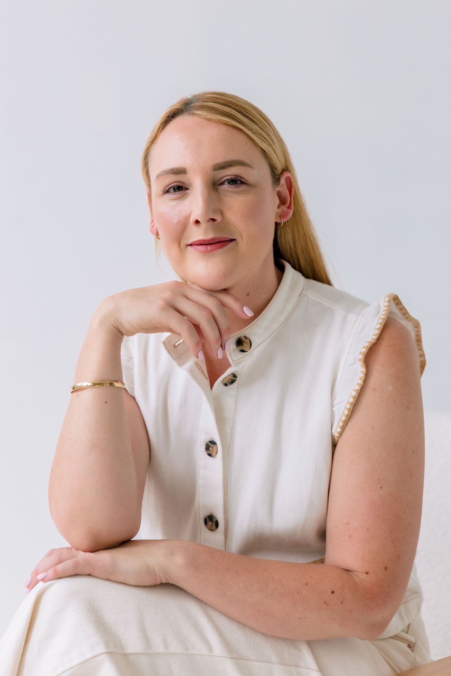 Model wearing a white sleeveless button-up top poses confidently against a light studio background.