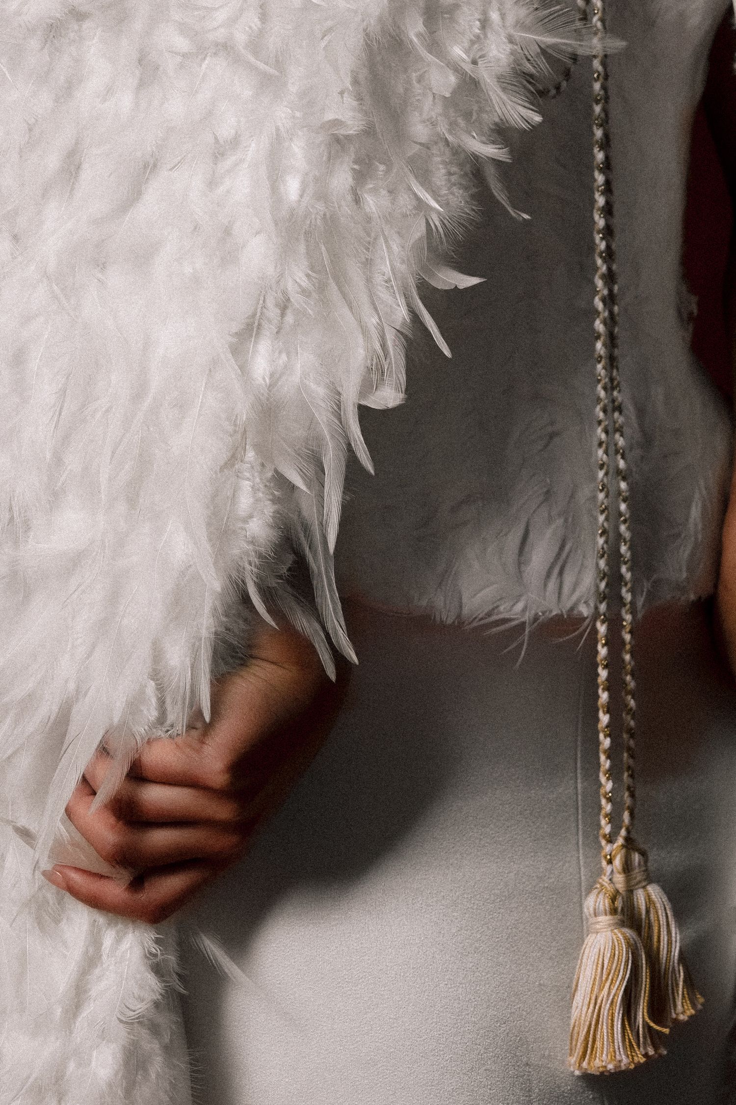 Close-up of a bride holding a white feather wrap with a braided tassel belt detail on a silver gown.