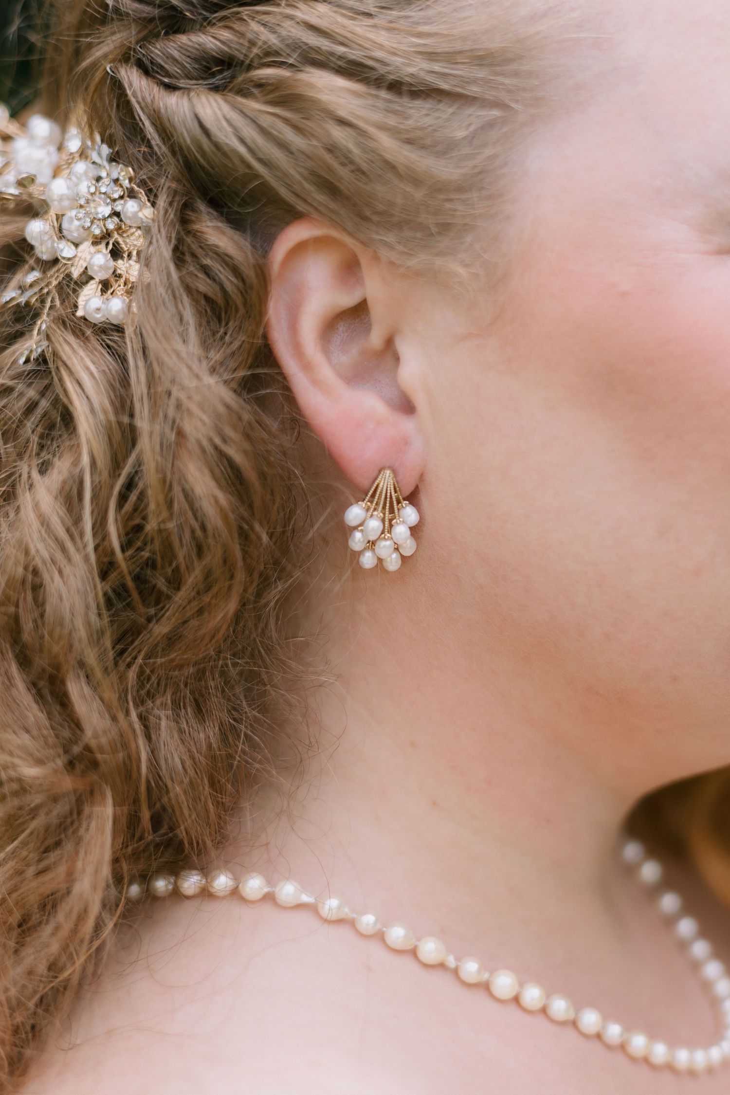 Close up of bridal jewelry showing delicate pearl earrings and hair accessories.