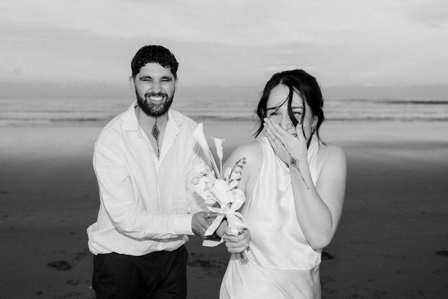 A candid beach wedding moment with white bouquet and casual attire.
