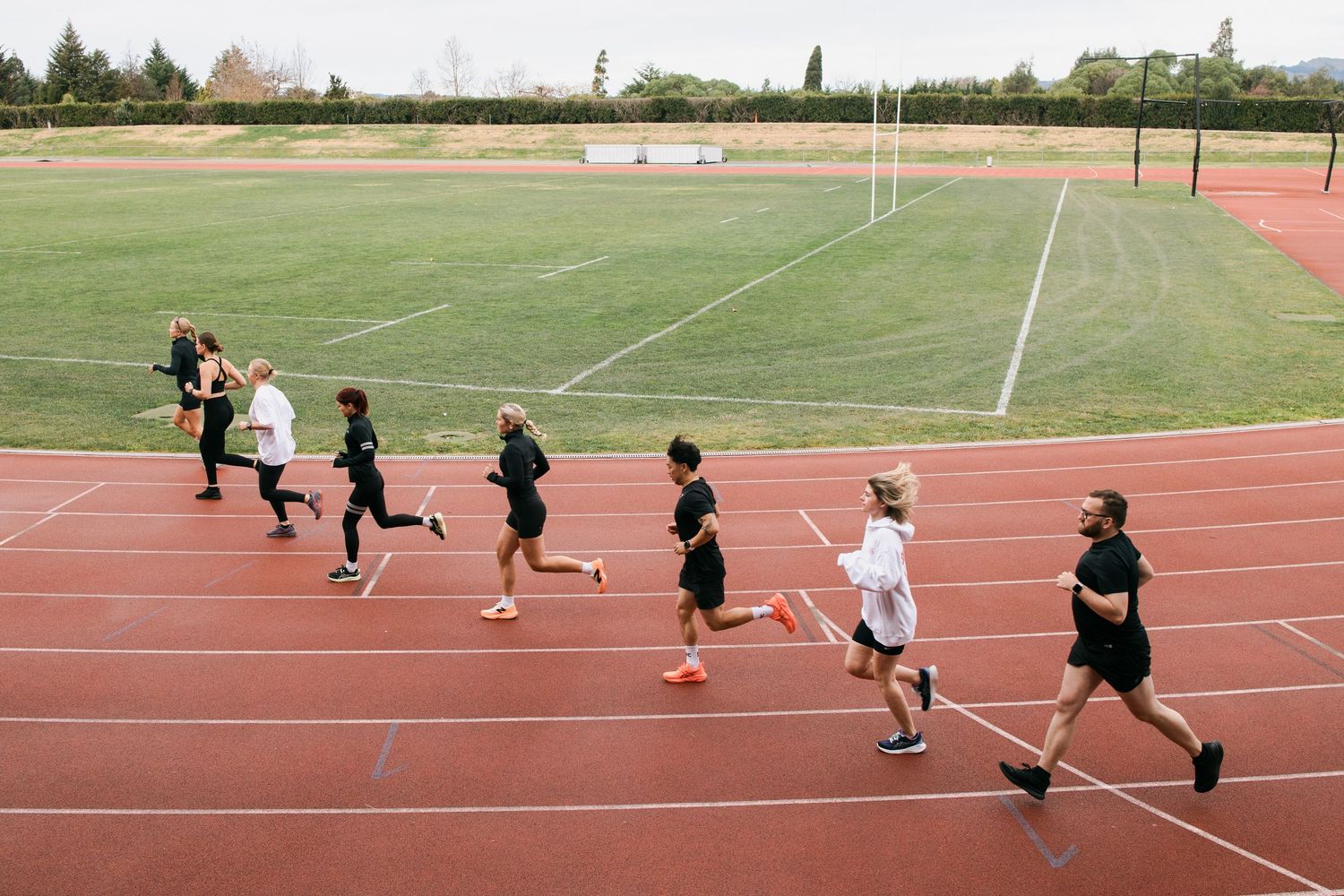 Athletes compete in a track race on a red running track next to a grass sports field.